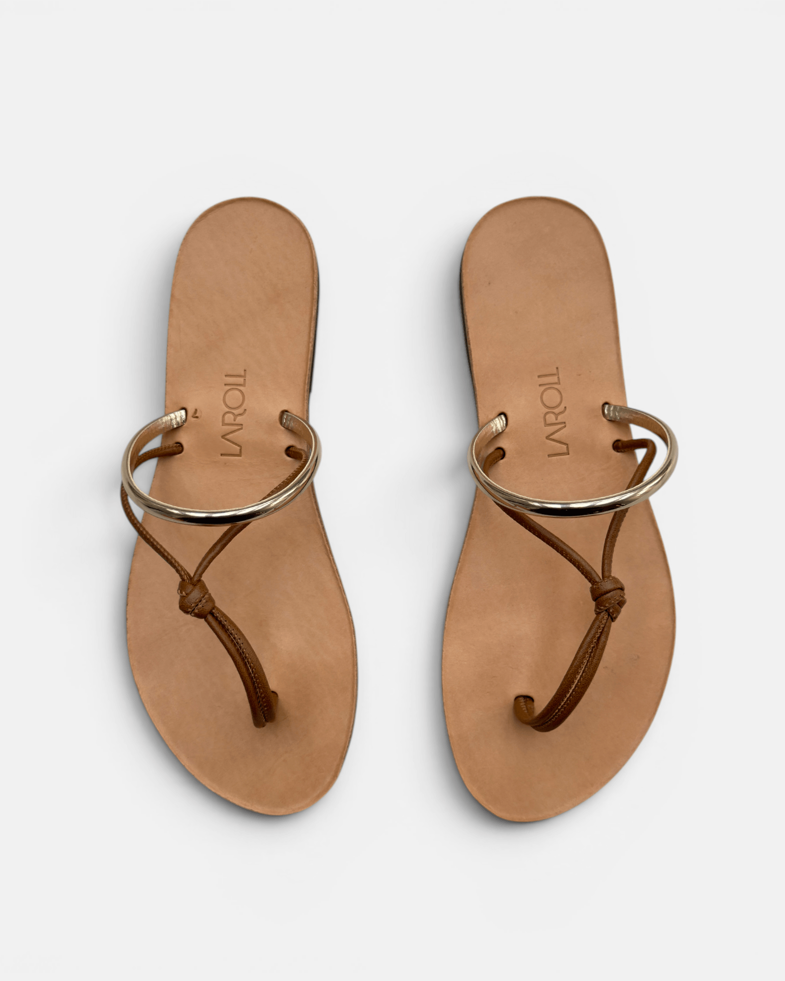 Pair of tan sandals with gold rings on a white background
