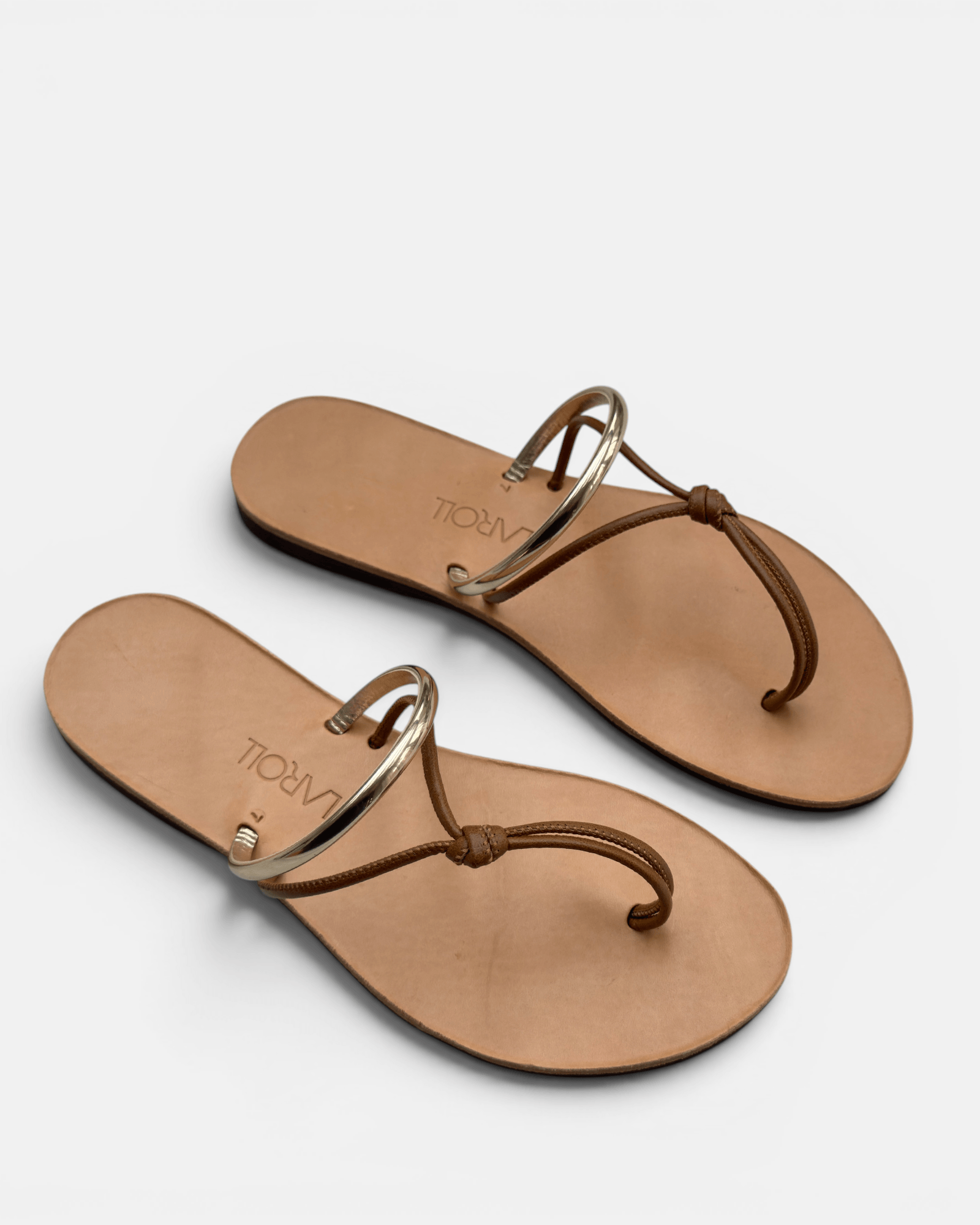 Pair of tan sandals with gold rings on a light gray background