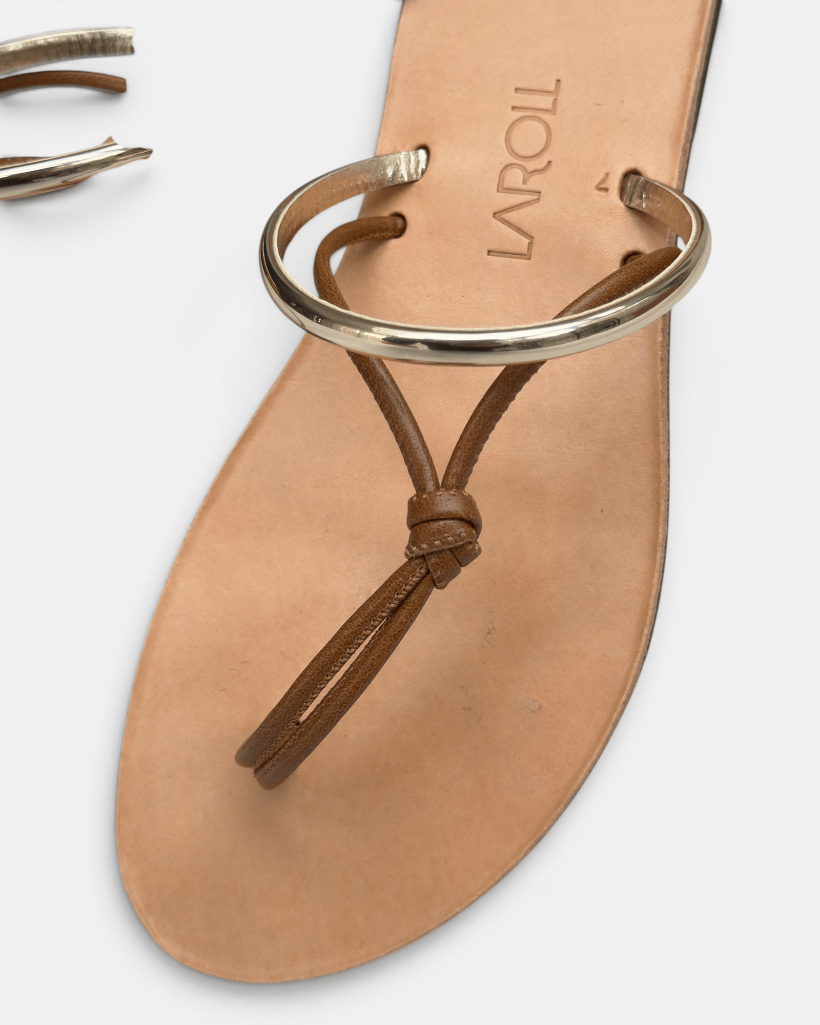 Tan sandal with gold ring thong on a white background