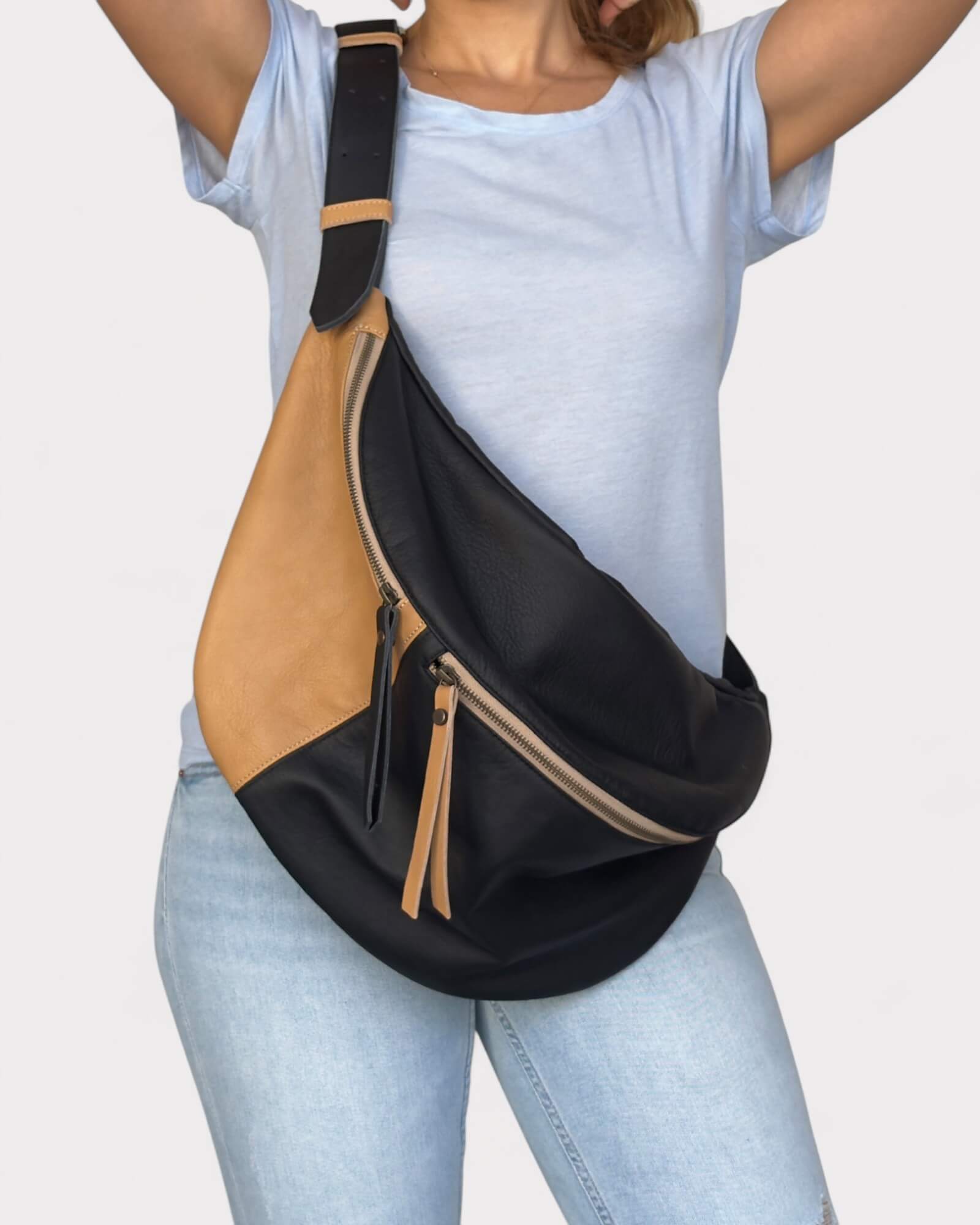 Person wearing a black and tan crossbody sling bag on a plain background