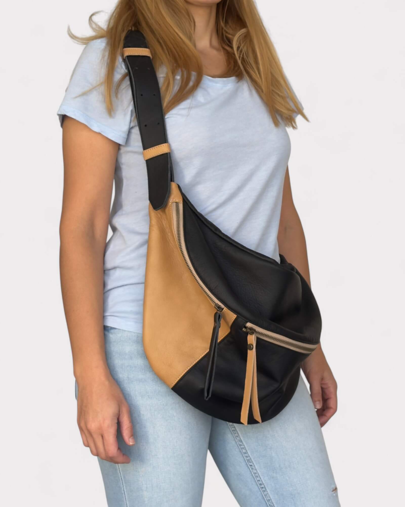 Model wearing a black and tan crossbody bag on a plain background