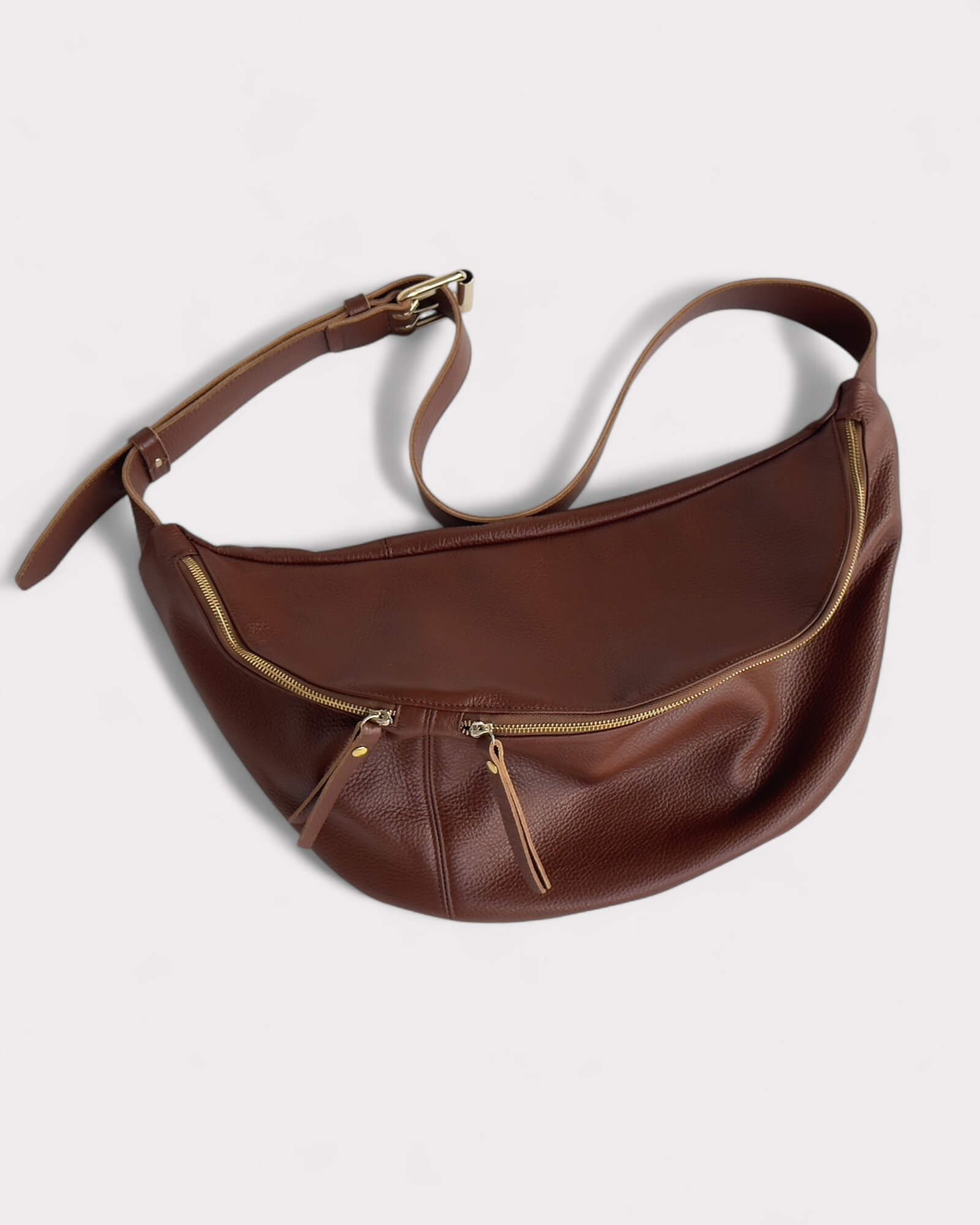Brown leather bag with gold zippers on a light gray background