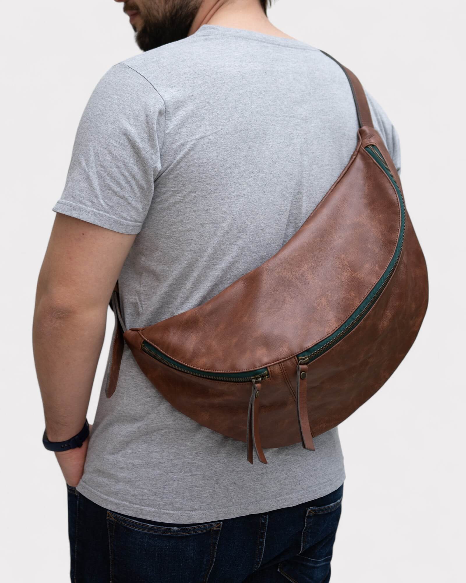 Man wearing a brown leather sling bag on a plain background