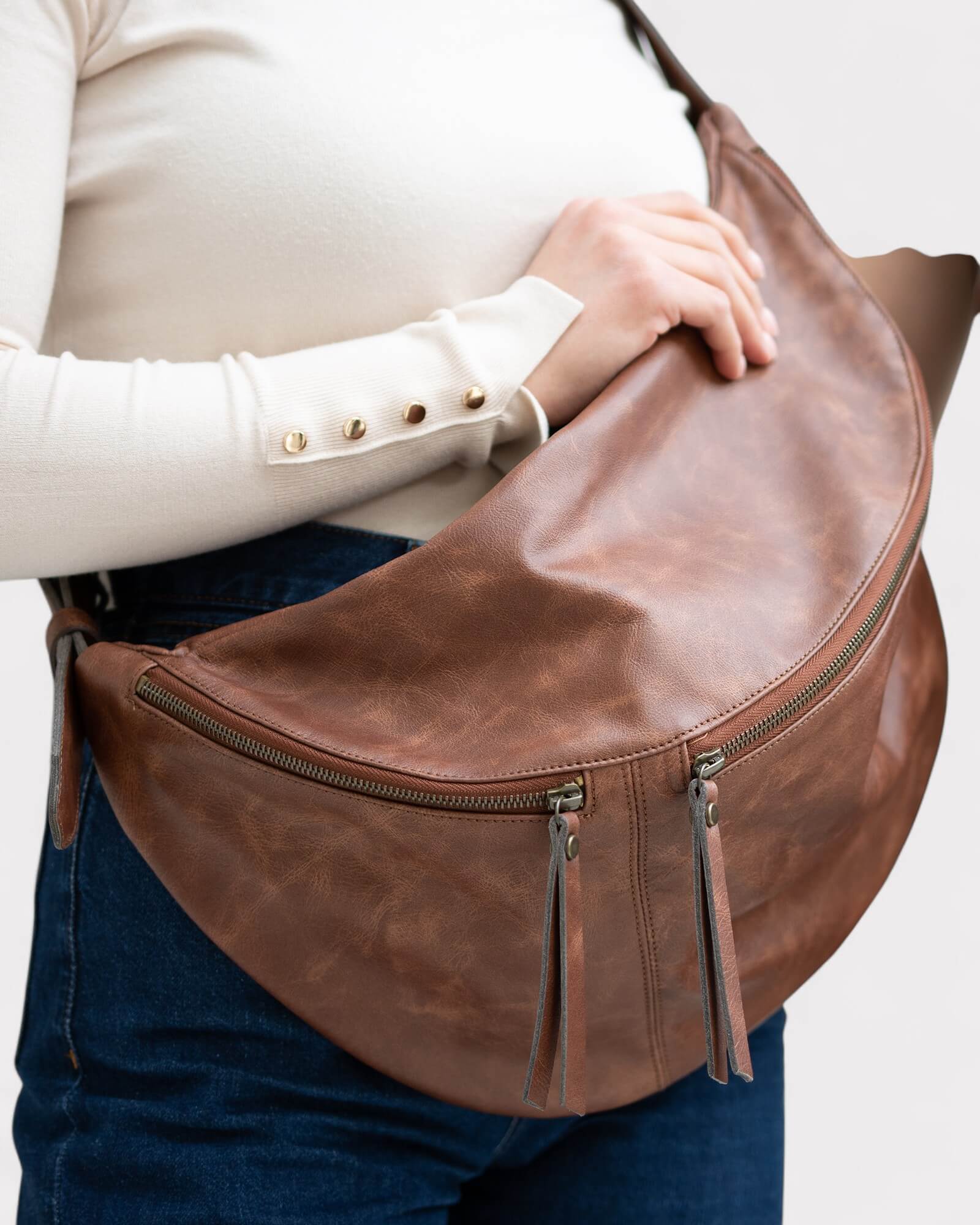 Brown leather sling bag worn over the shoulder on a plain background