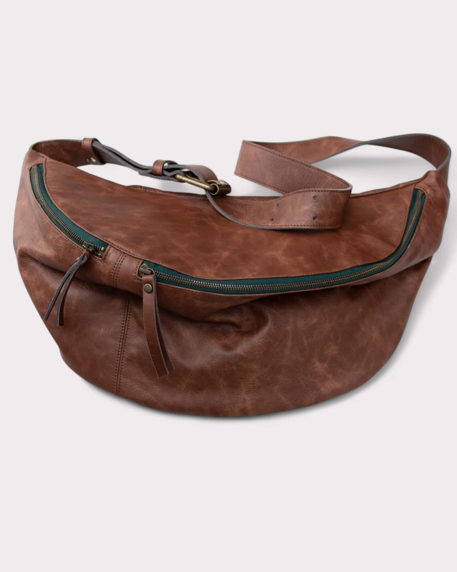 Brown leather waist bag with green zippers on a light gray background