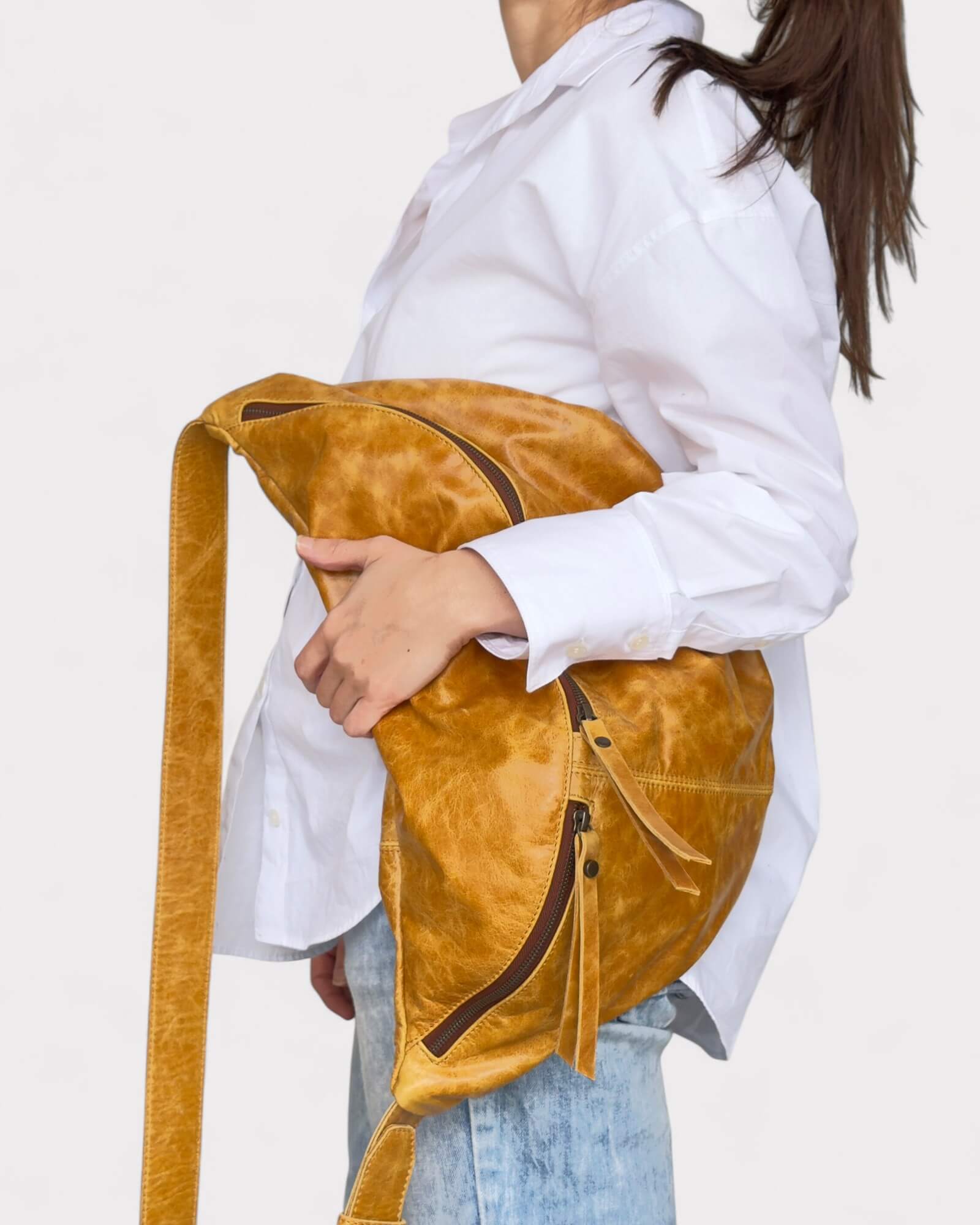 Person holding a tan leather bag with a white shirt and light blue jeans on a plain background