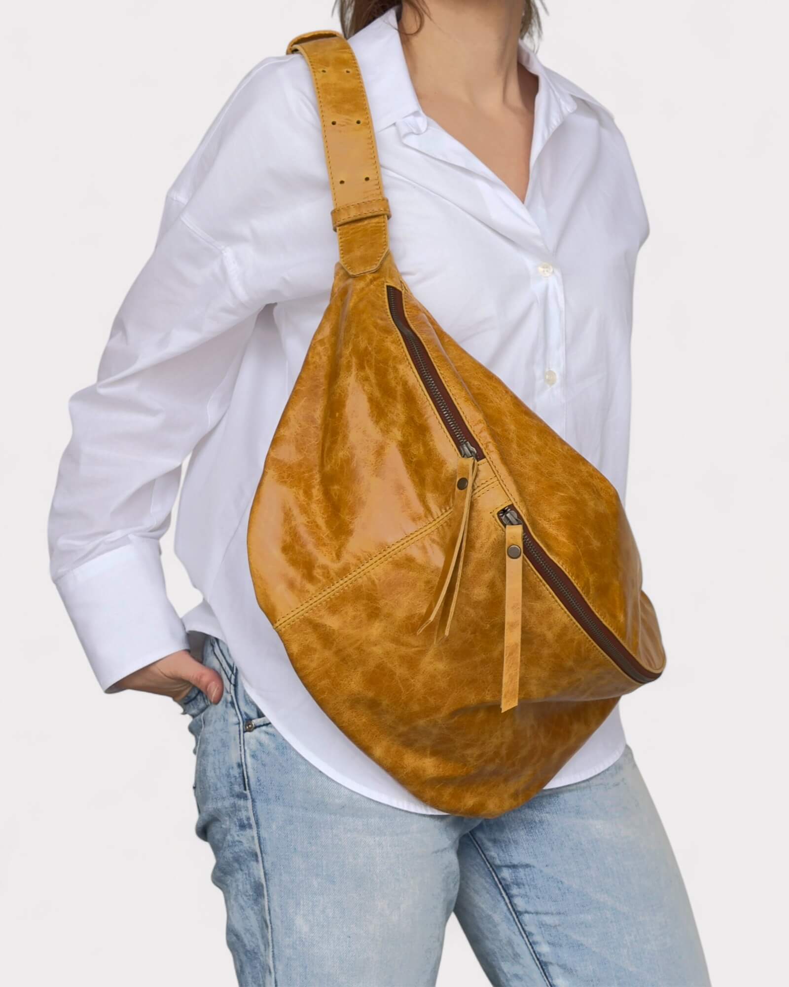Model wearing a tan leather sling bag on a white background