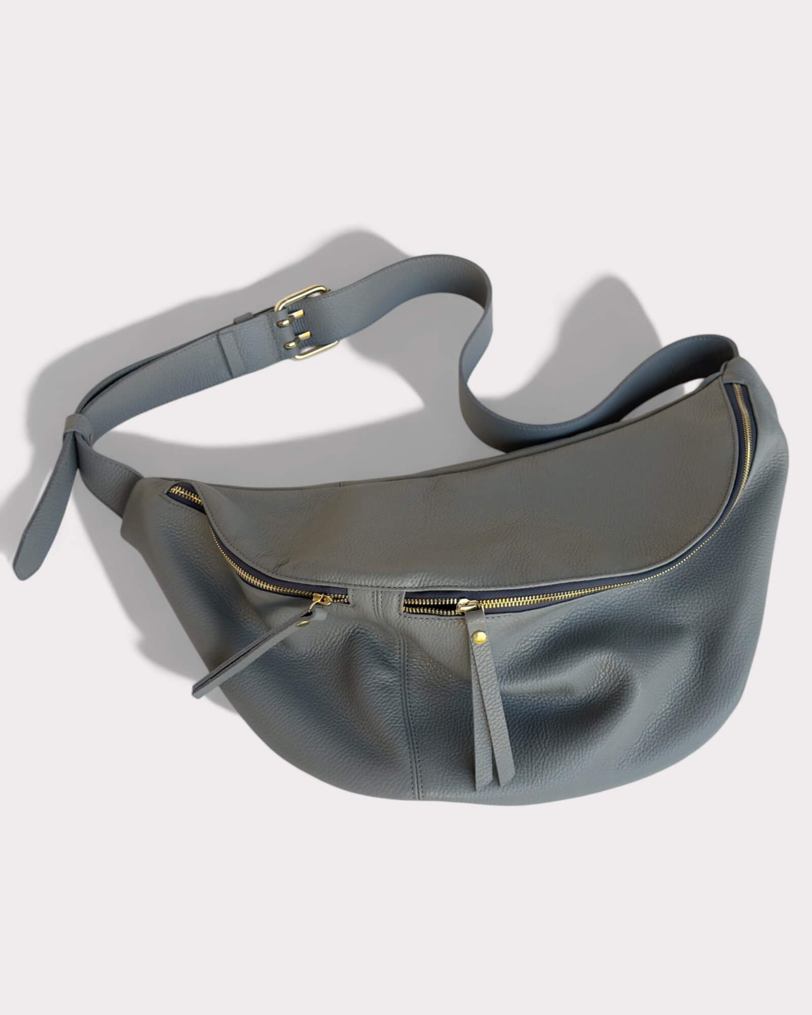 Gray leather waist bag with gold zipper on a light gray background