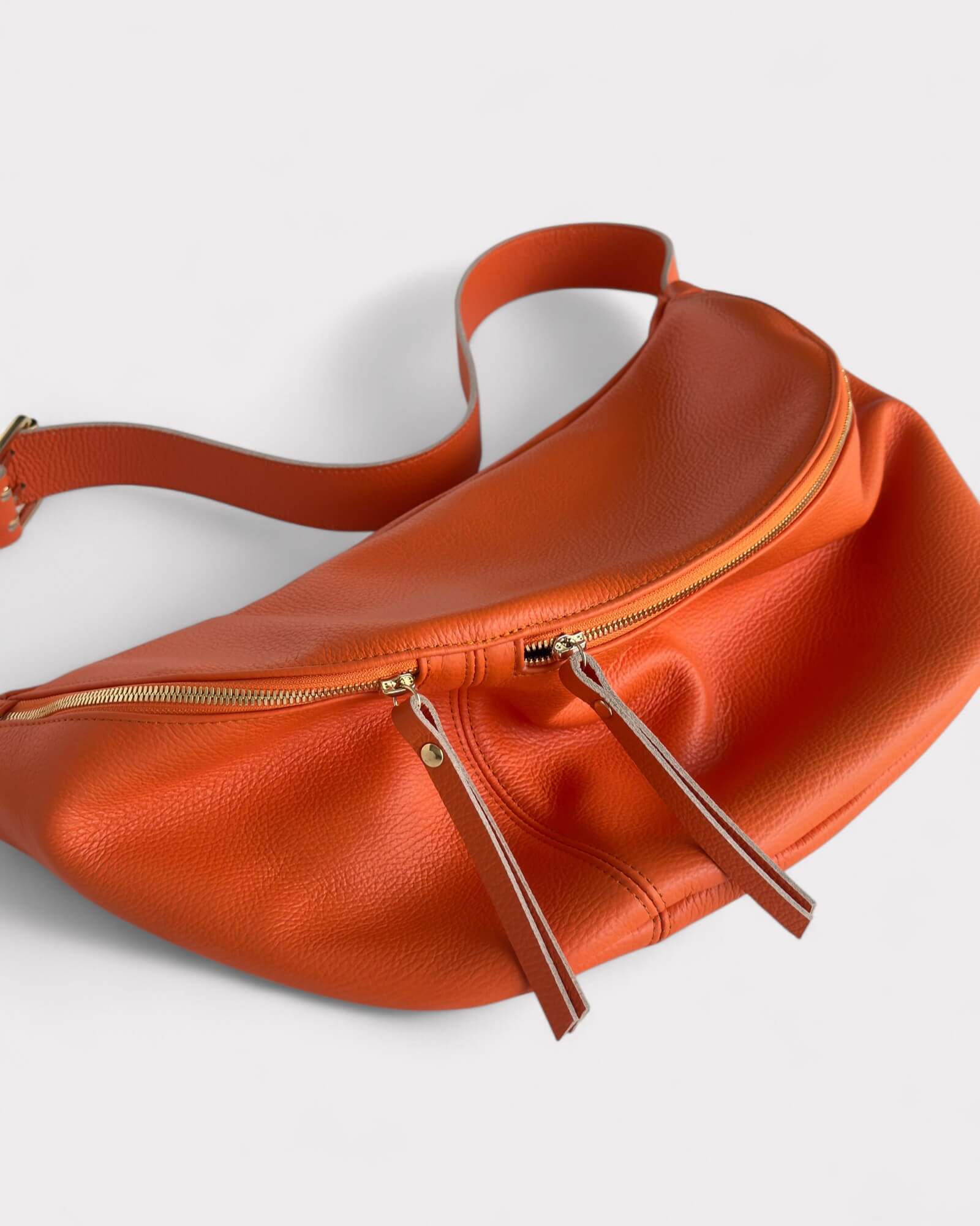 Orange leather waist bag with gold zippers on a light gray background