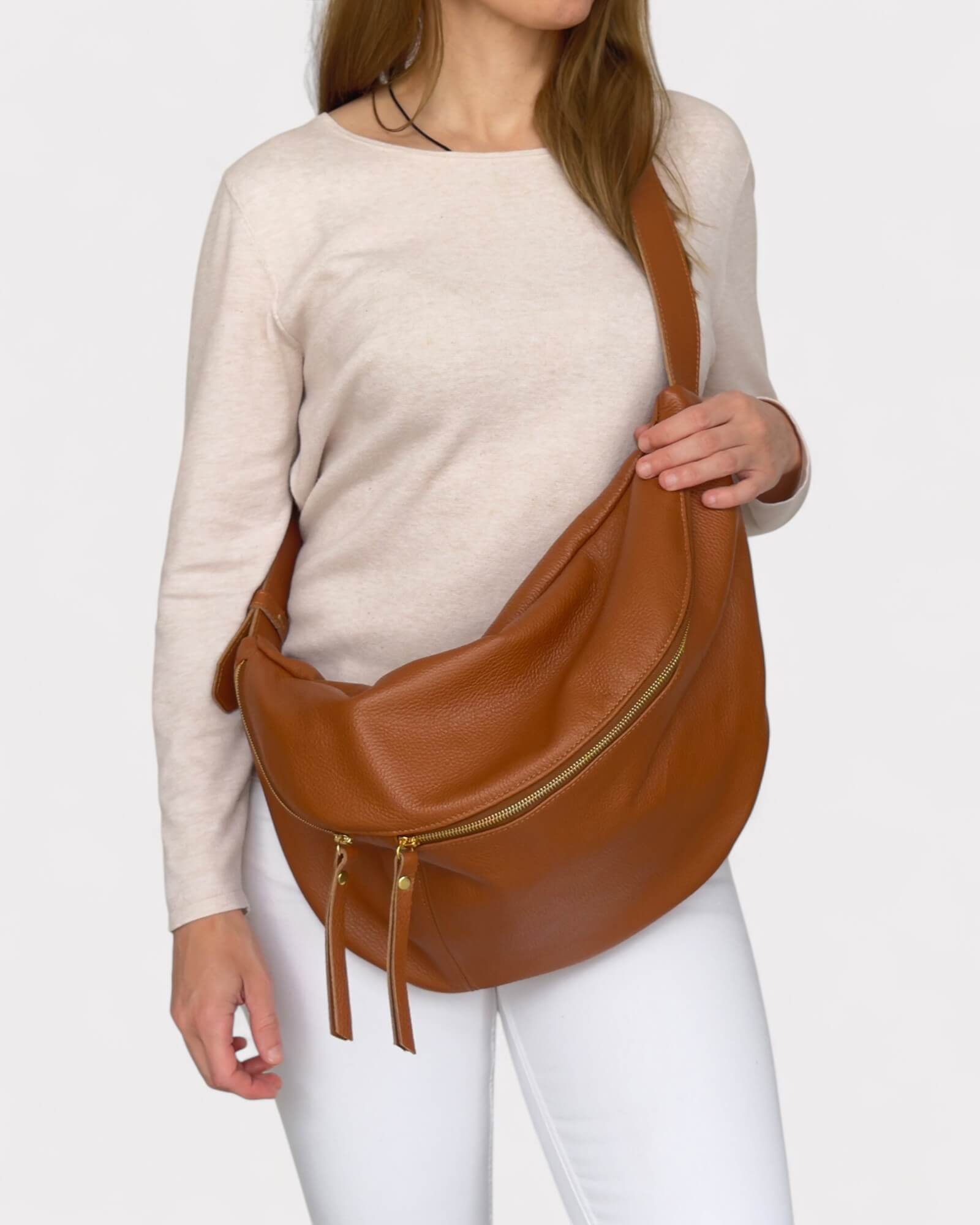 Woman wearing a tan leather bag on a plain background