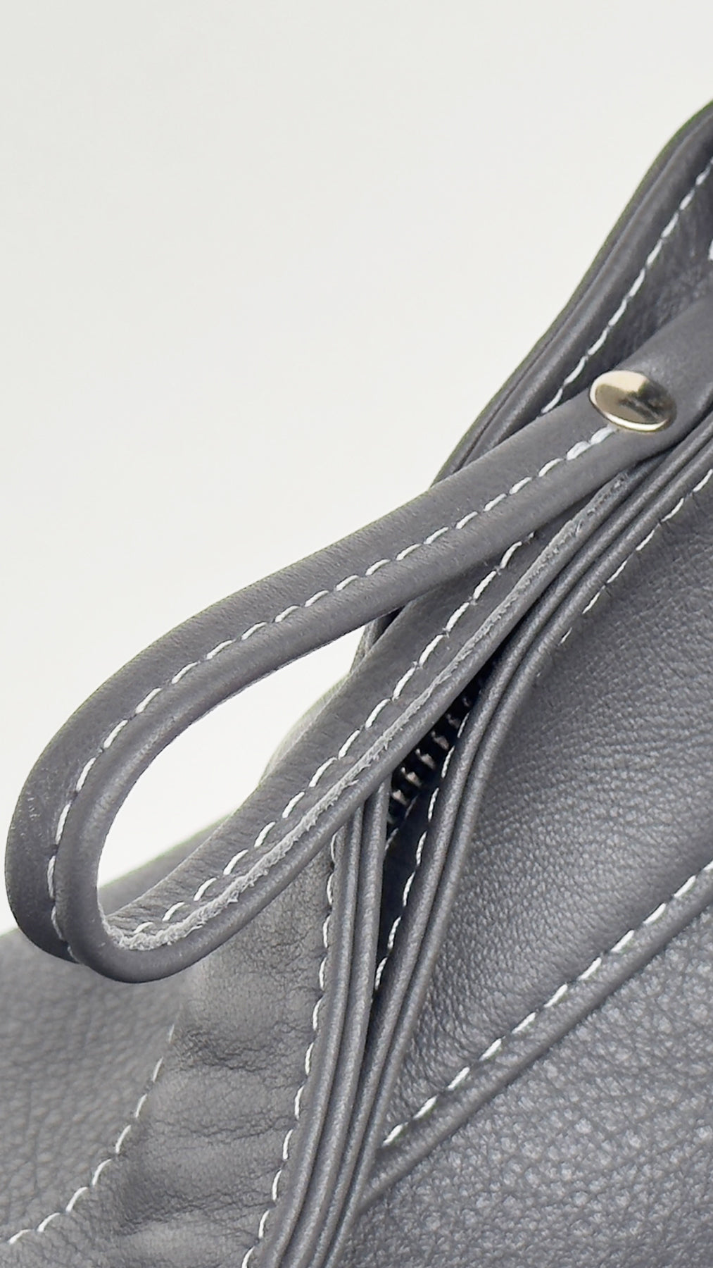 Close-up of a gray leather handbag handle with stitching detail on a light gray background