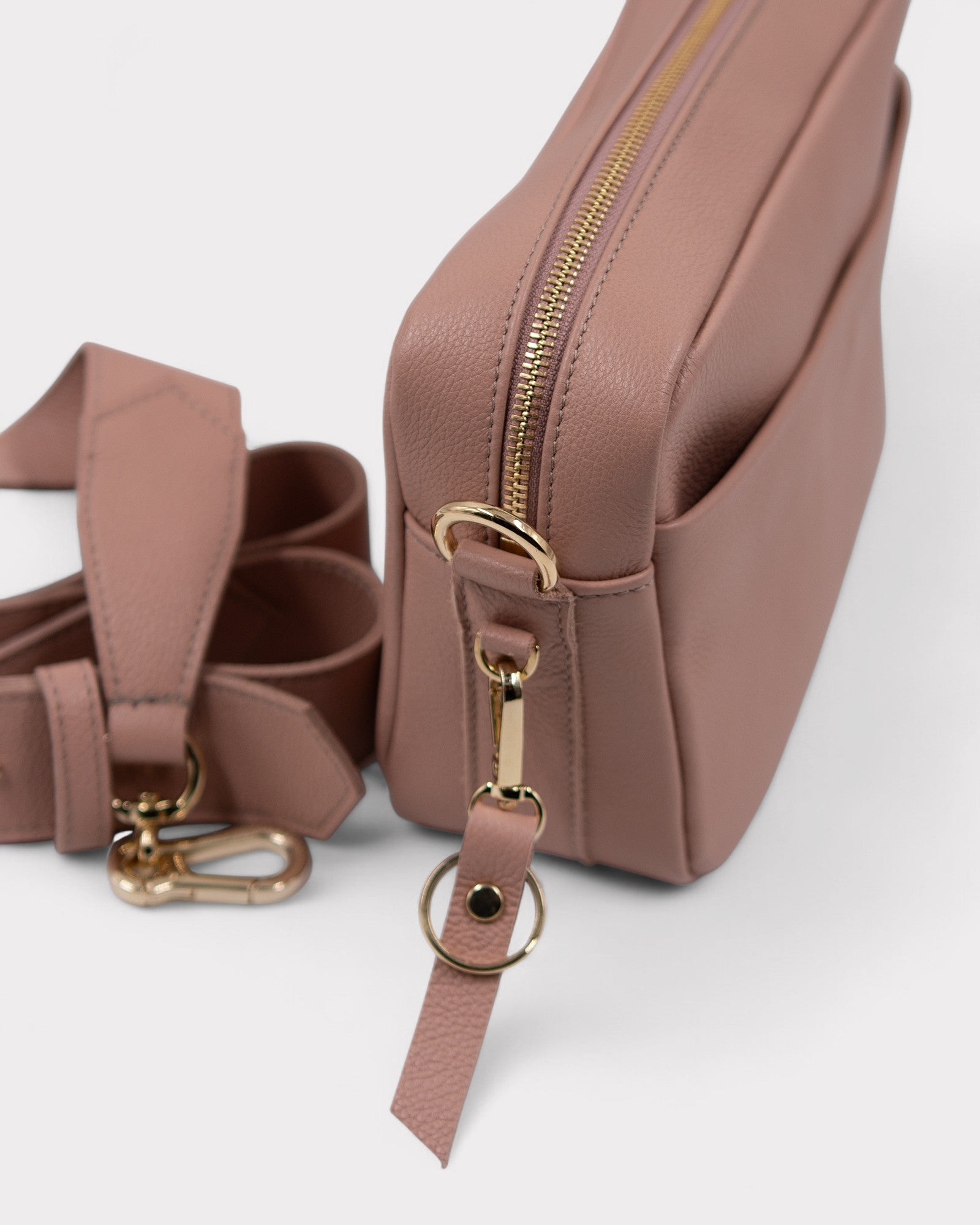 dusty rose leather bag with gold zipper and strap on a white background