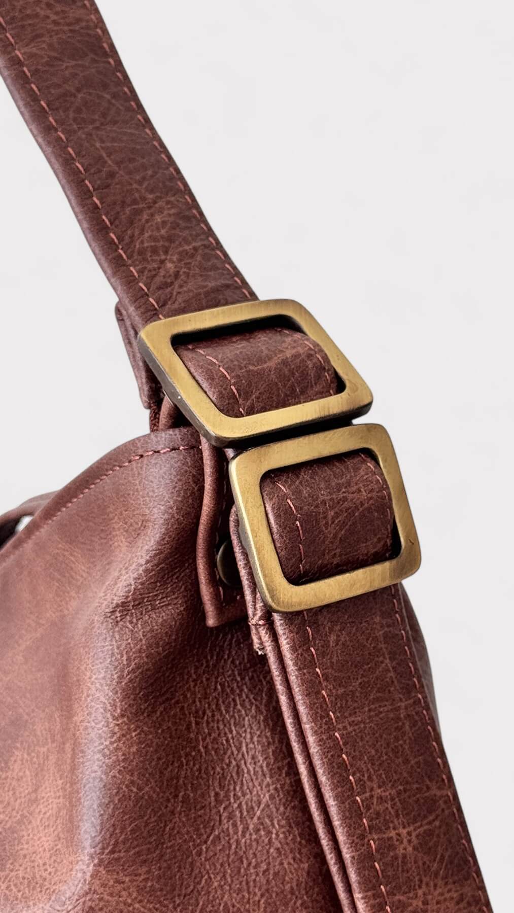 Brown leather handbag with bronze hardware on a white background