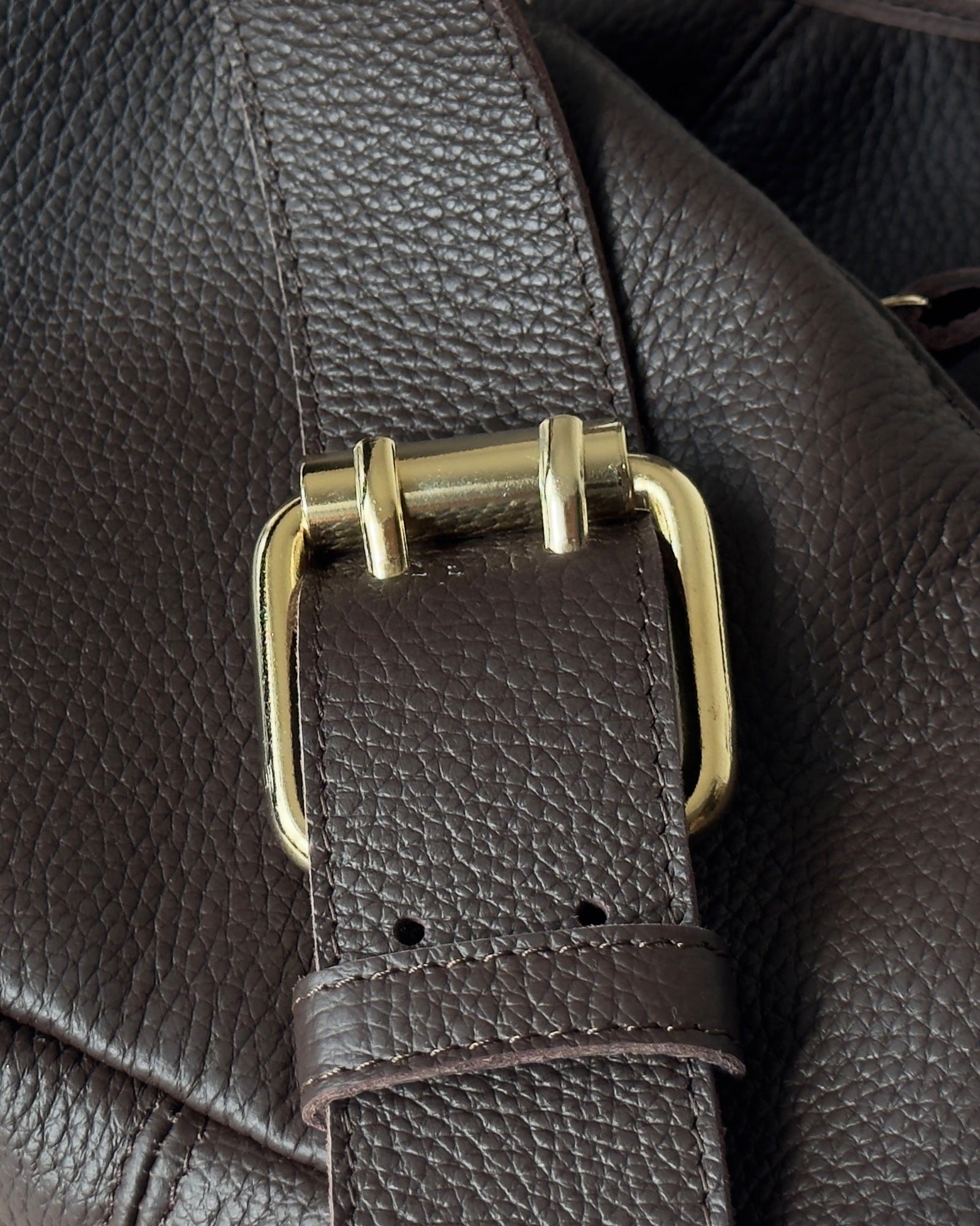 Close-up of a brown leather strap with a gold buckle on a textured surface.