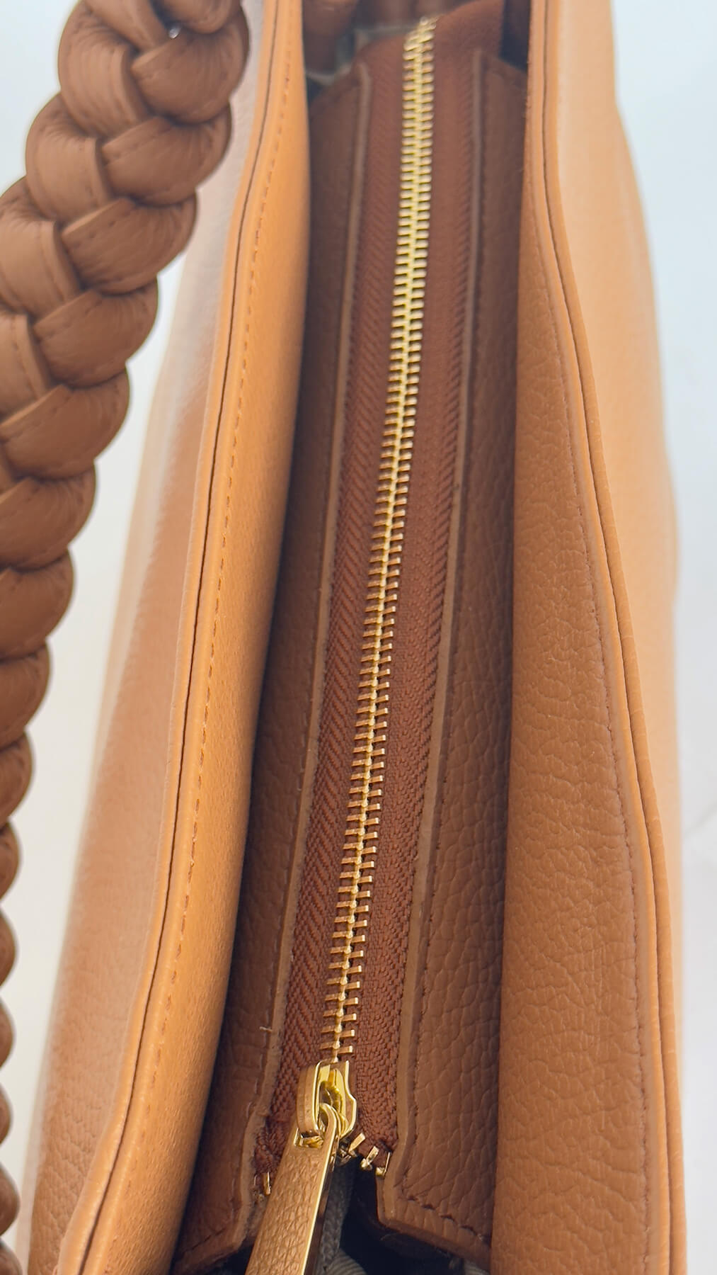 Close-up of a tan leather bag with a gold zipper on a light blue background