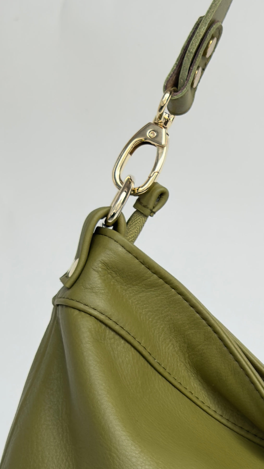 Close-up of a green leather handbag with a gold clasp on a light gray background