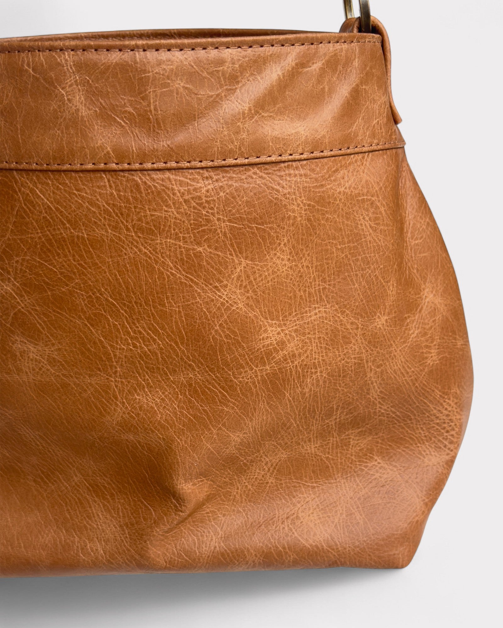 Close-up of a tan distressed leather handbag on a light gray background