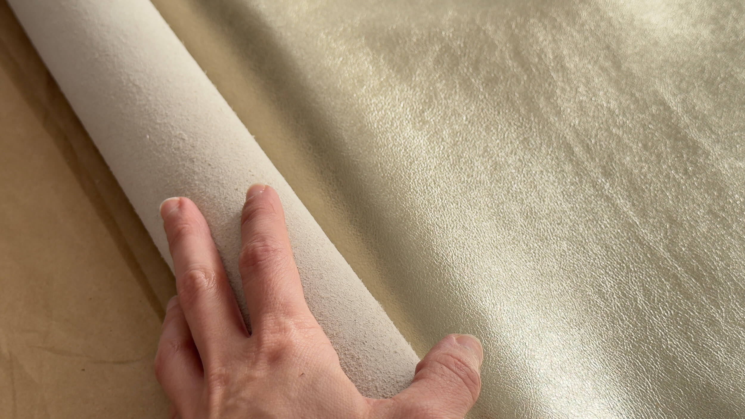 Hand unfolding a gold leather hide inside workshop