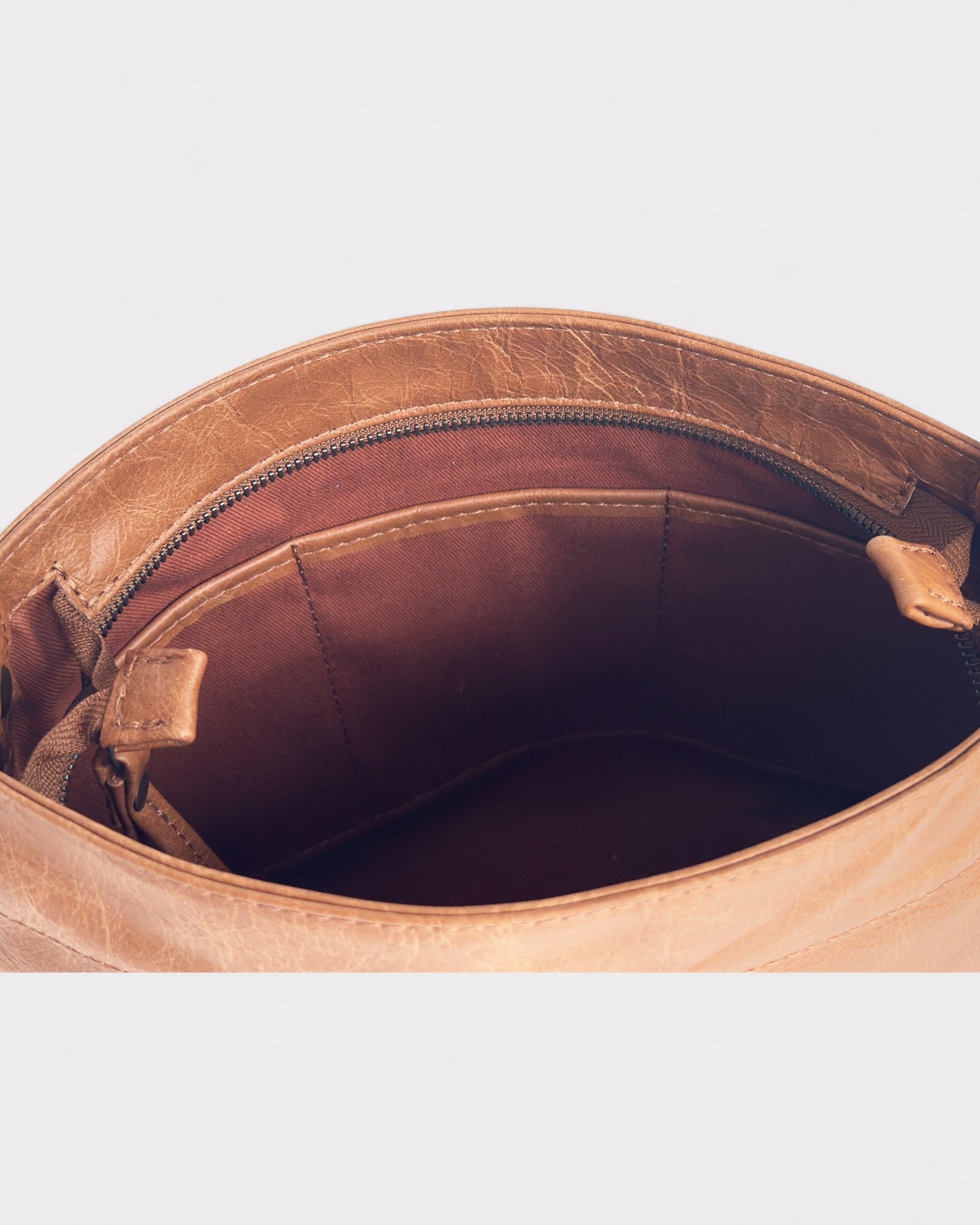 Close-up of a tan distressed leather bag with a zipper on a light gray background