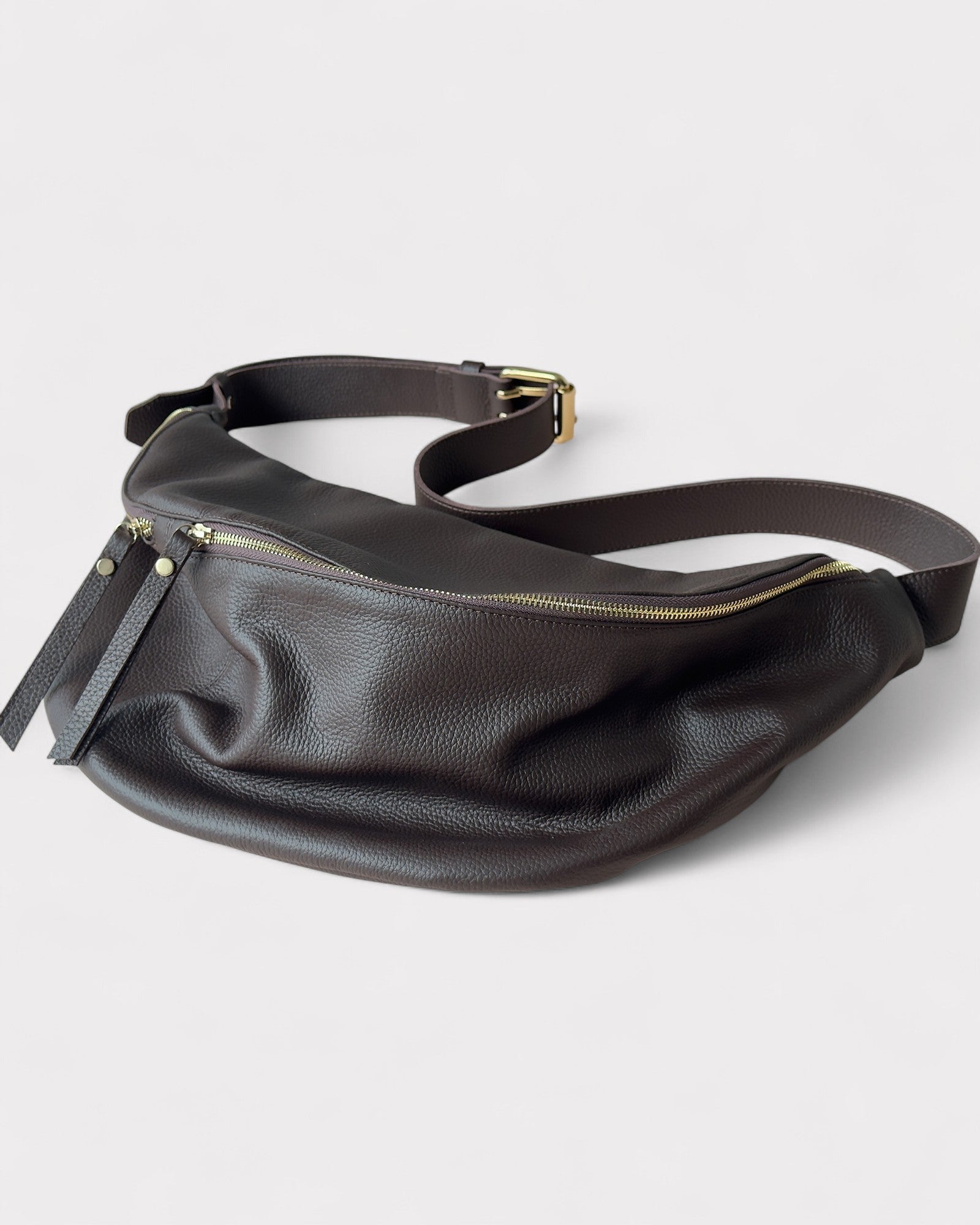 Brown leather waist bag with gold zipper on a light gray background