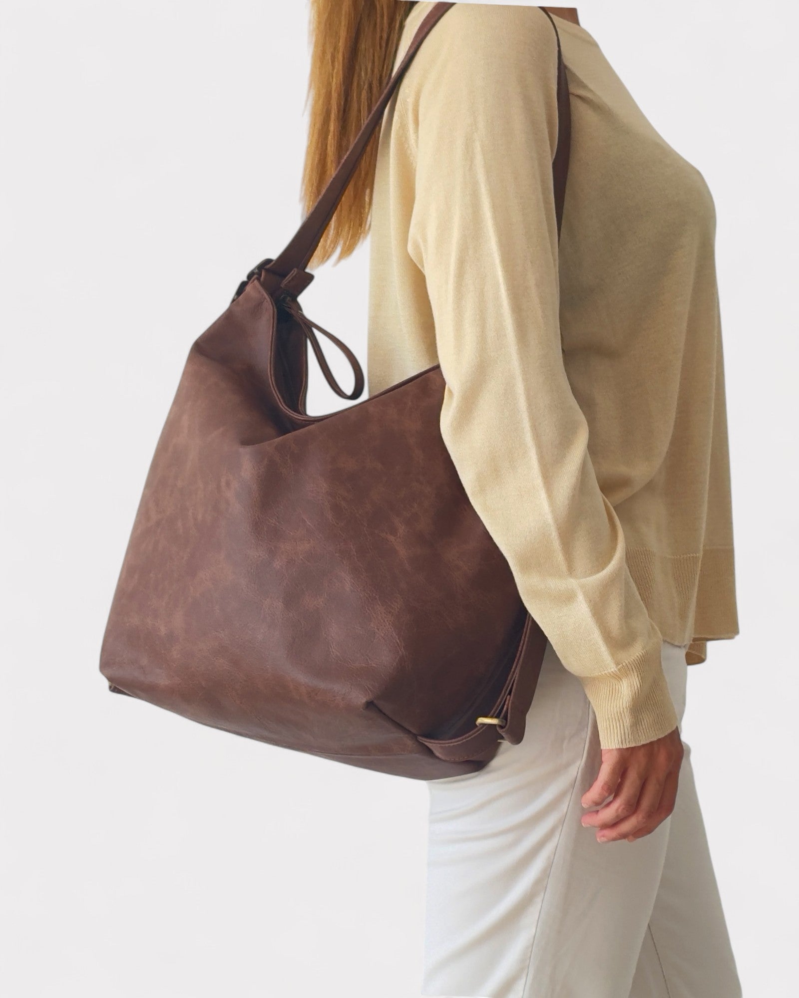 Person wearing a brown leather shoulder bag on a white background