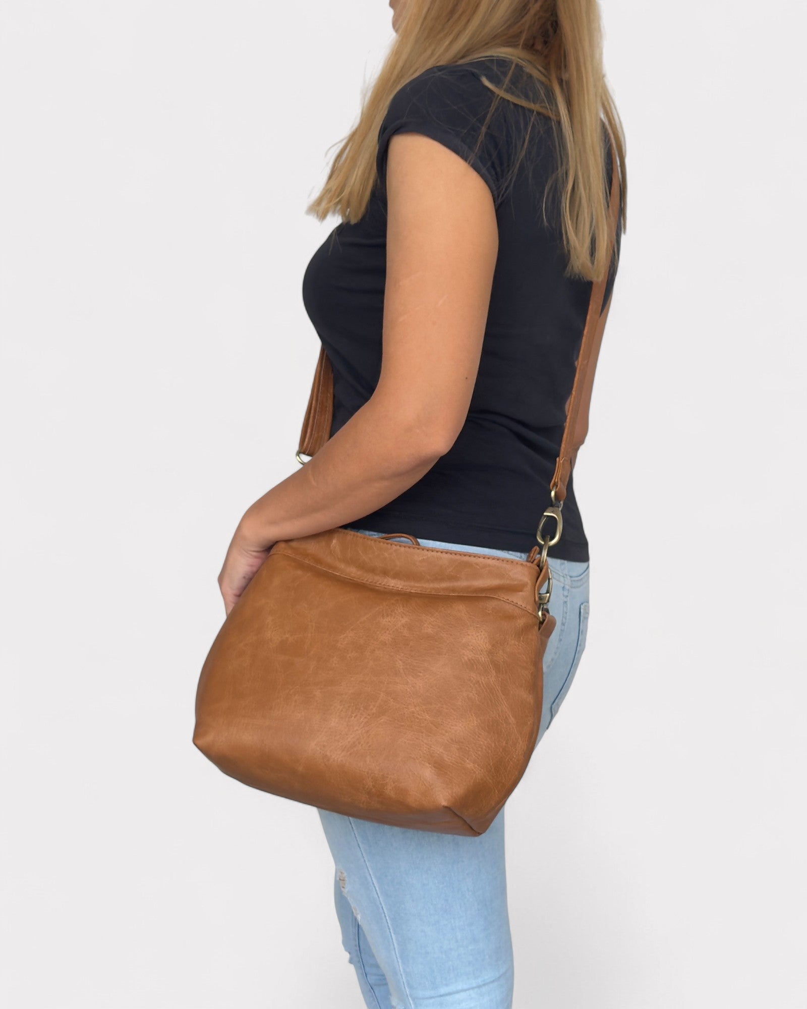 Woman holding a tan distressed leather handbag against a plain background