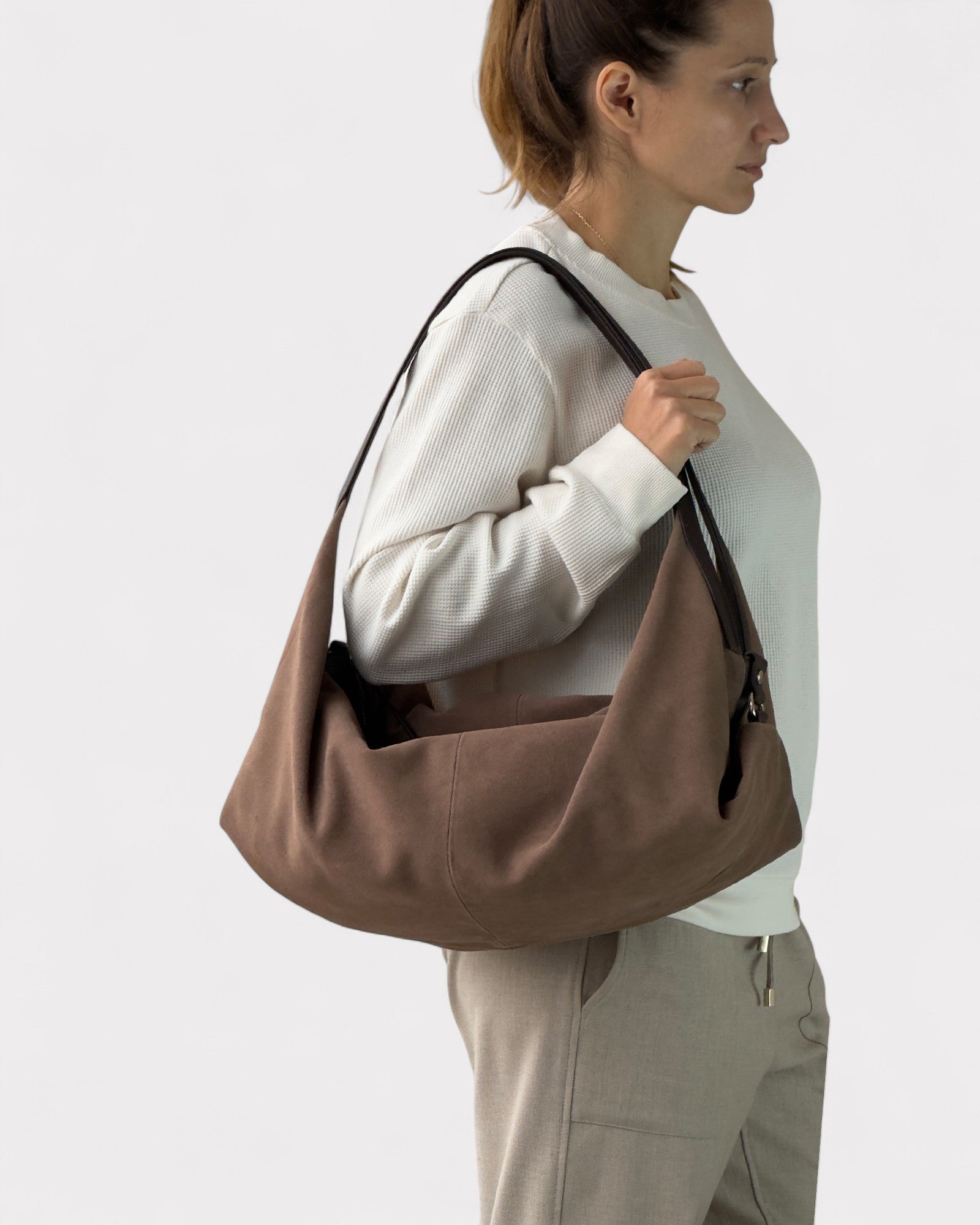 Woman carrying a taupe shoulder bag on a plain background