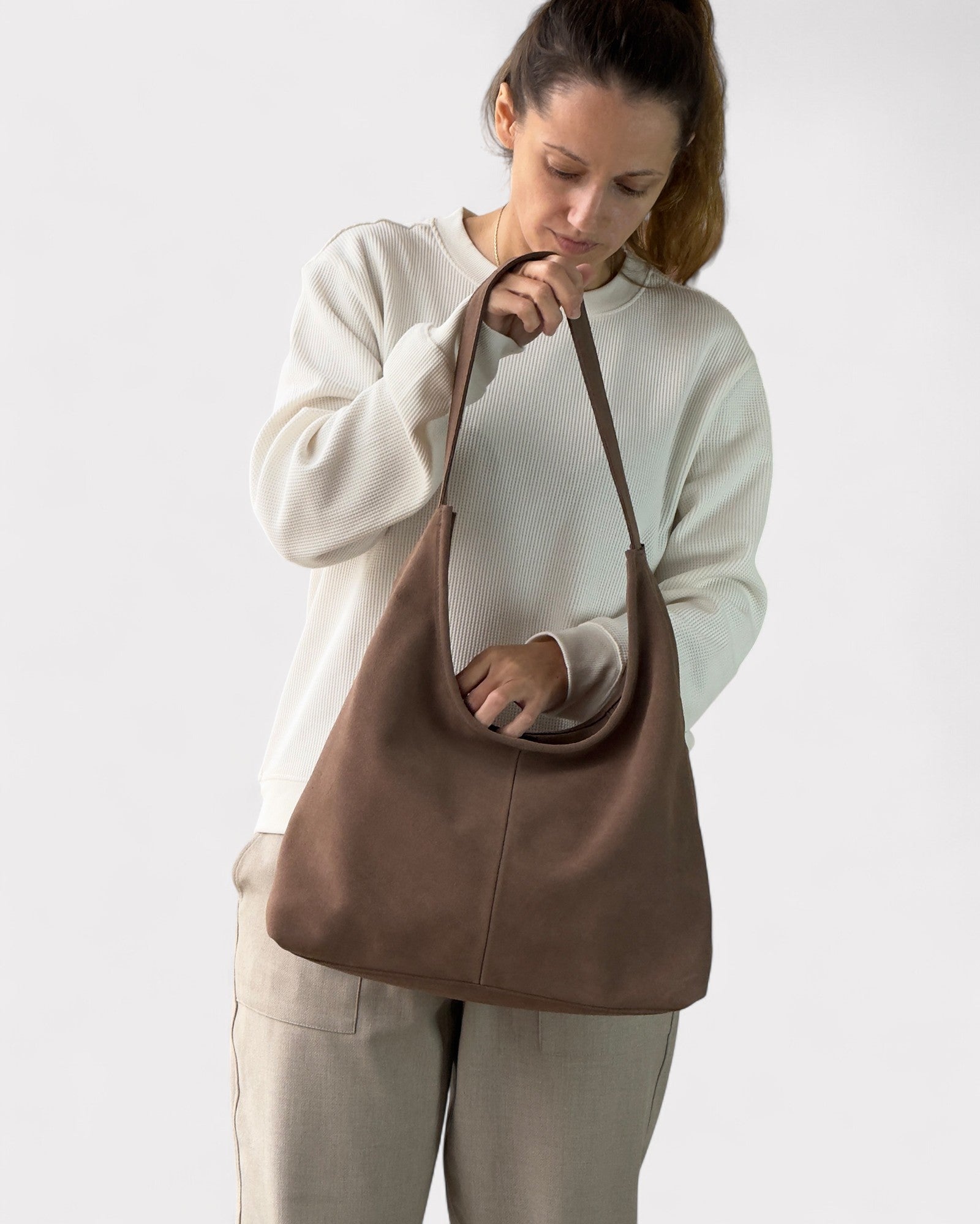 Woman holding a taupe leather bag against a white background