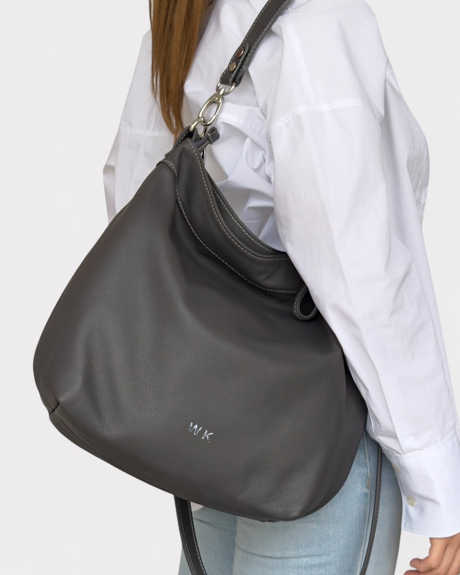 Person wearing a gray shoulder bag with monogram on a white background
