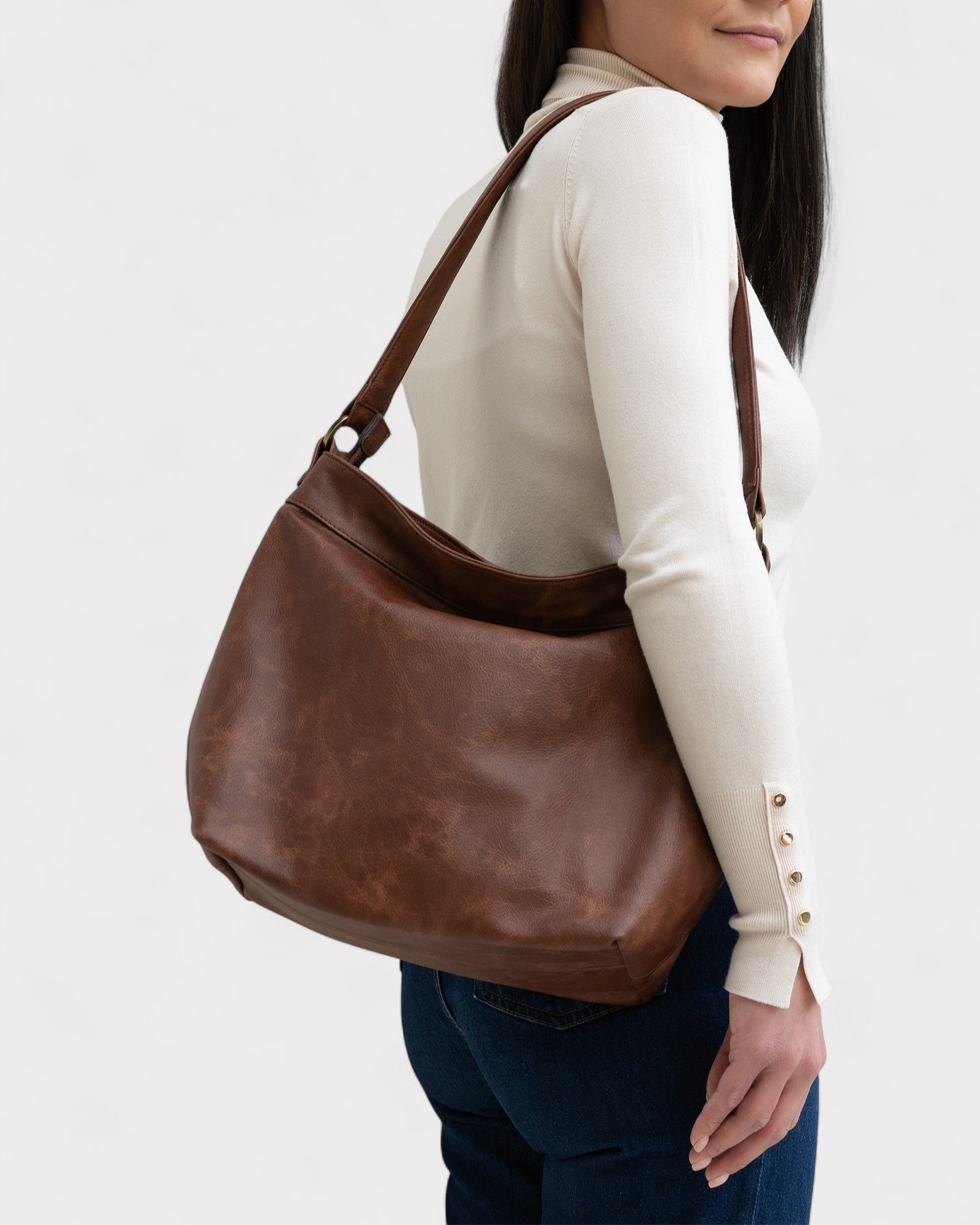 Woman carrying a brown leather handbag on a plain background