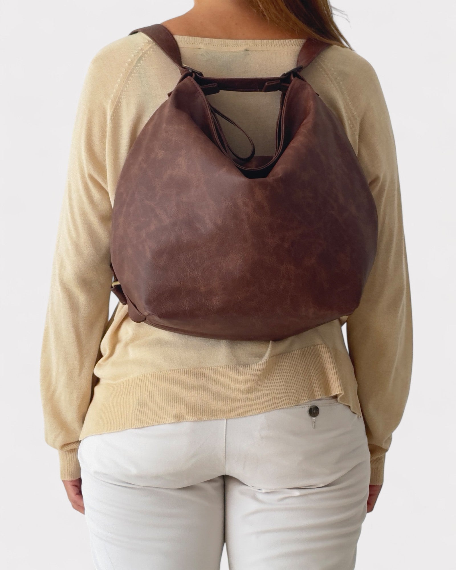 Person wearing a brown leather backpack on a plain background