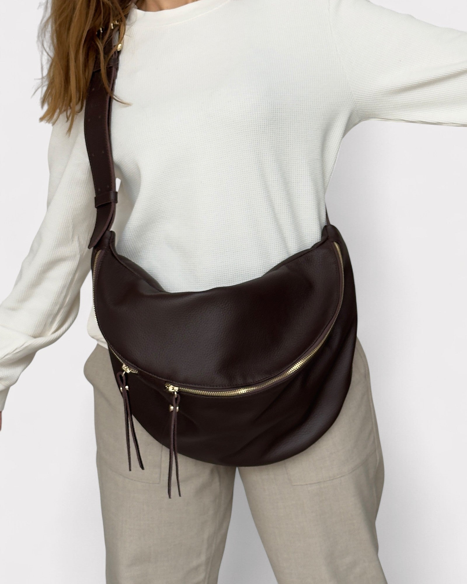 Person wearing a brown leather waist bag on a plain background