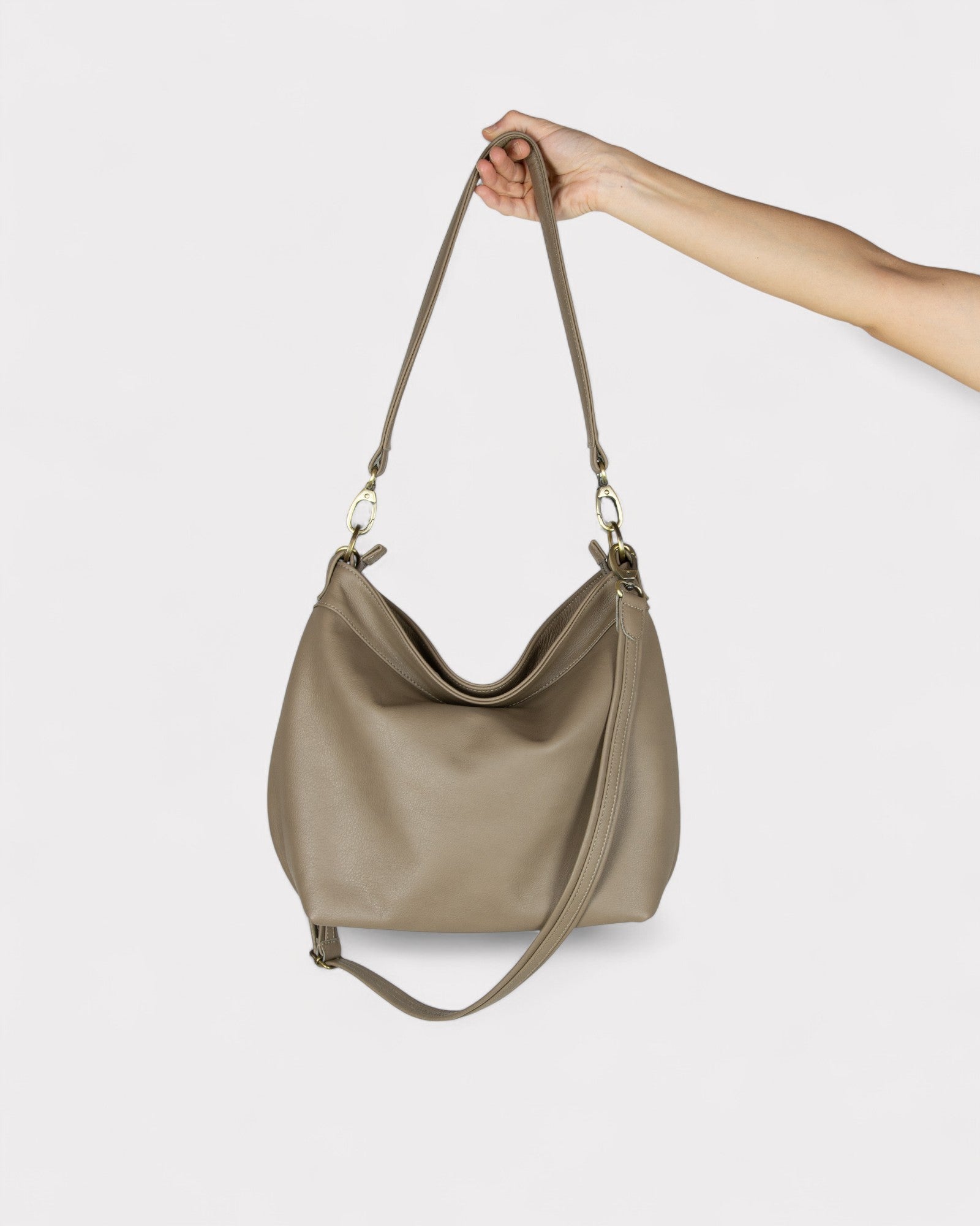 taupe handbag held by a hand against a white background