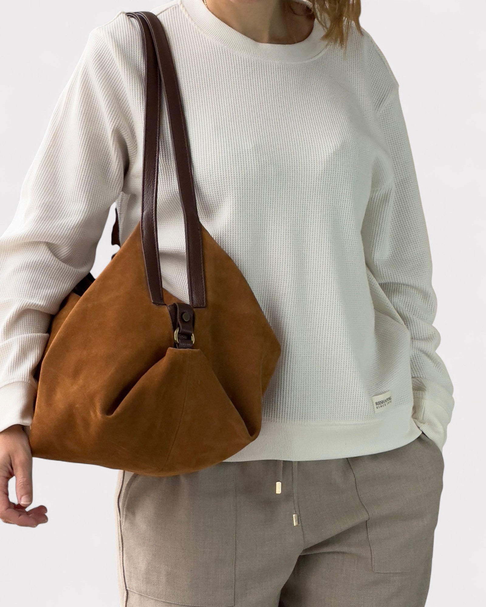 Person wearing a white sweater and brown pants holding a tan leather handbag.