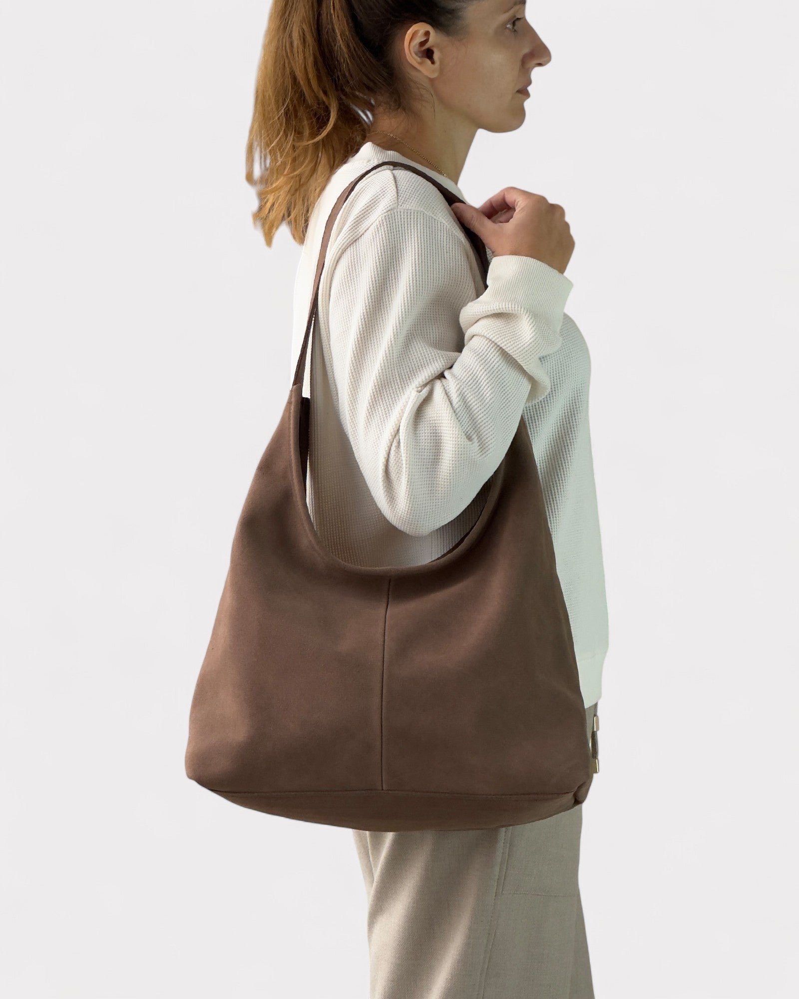 Woman carrying a taupe leather bag on a plain background
