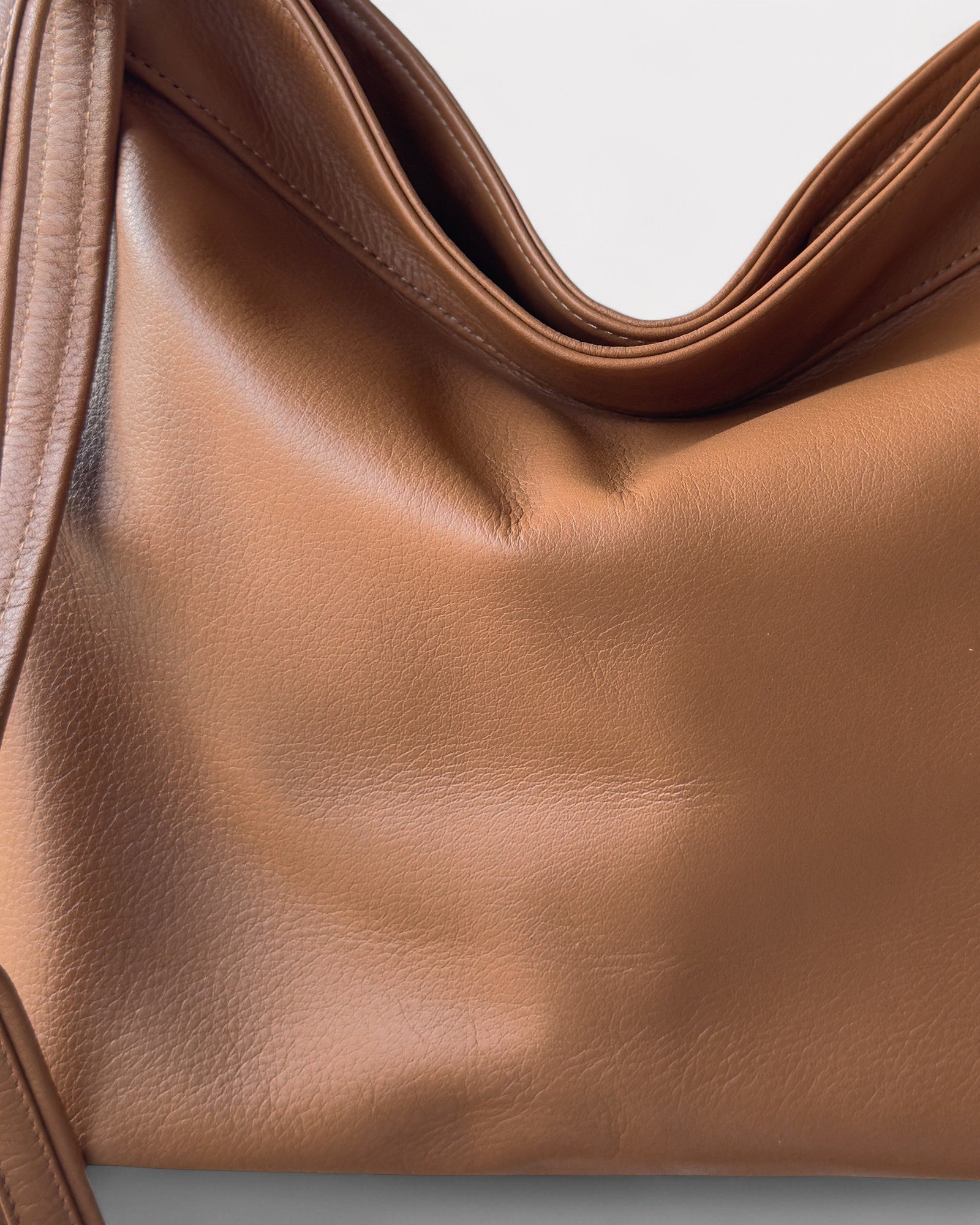 Close-up of a tan leather handbag with a light gray background