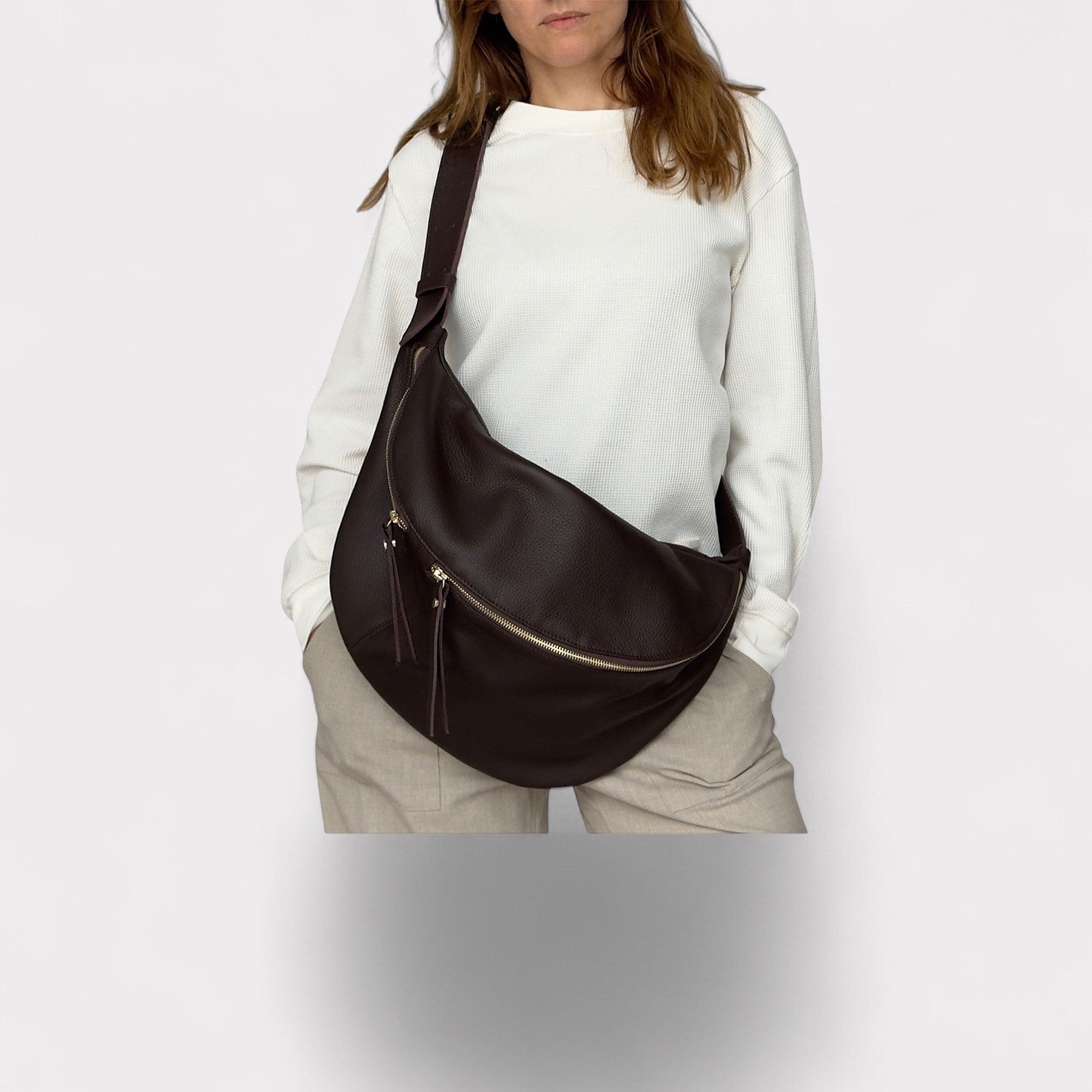 Person wearing a brown shoulder bag on a plain background