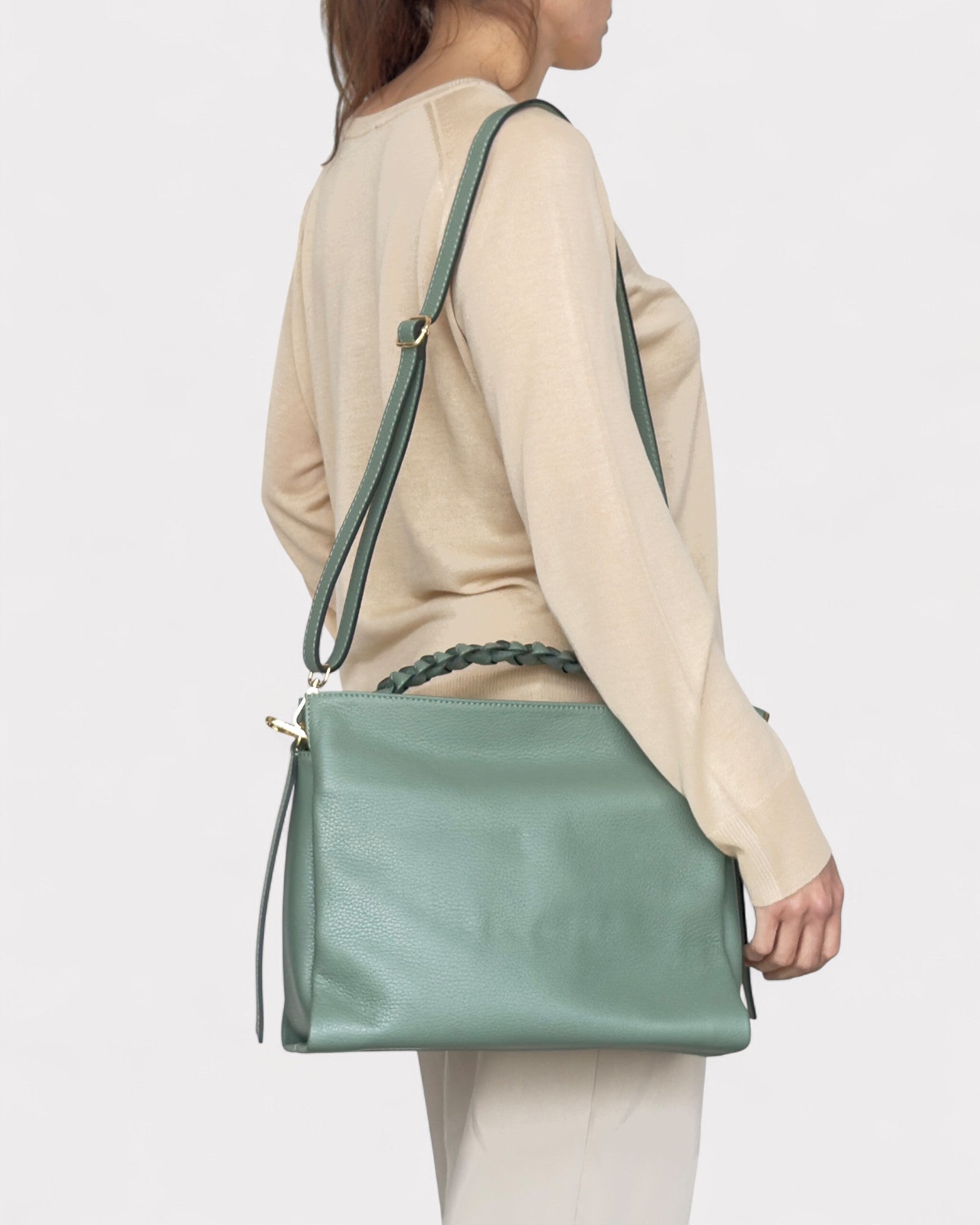 Person wearing a light beige sweater and holding a green handbag on a plain background