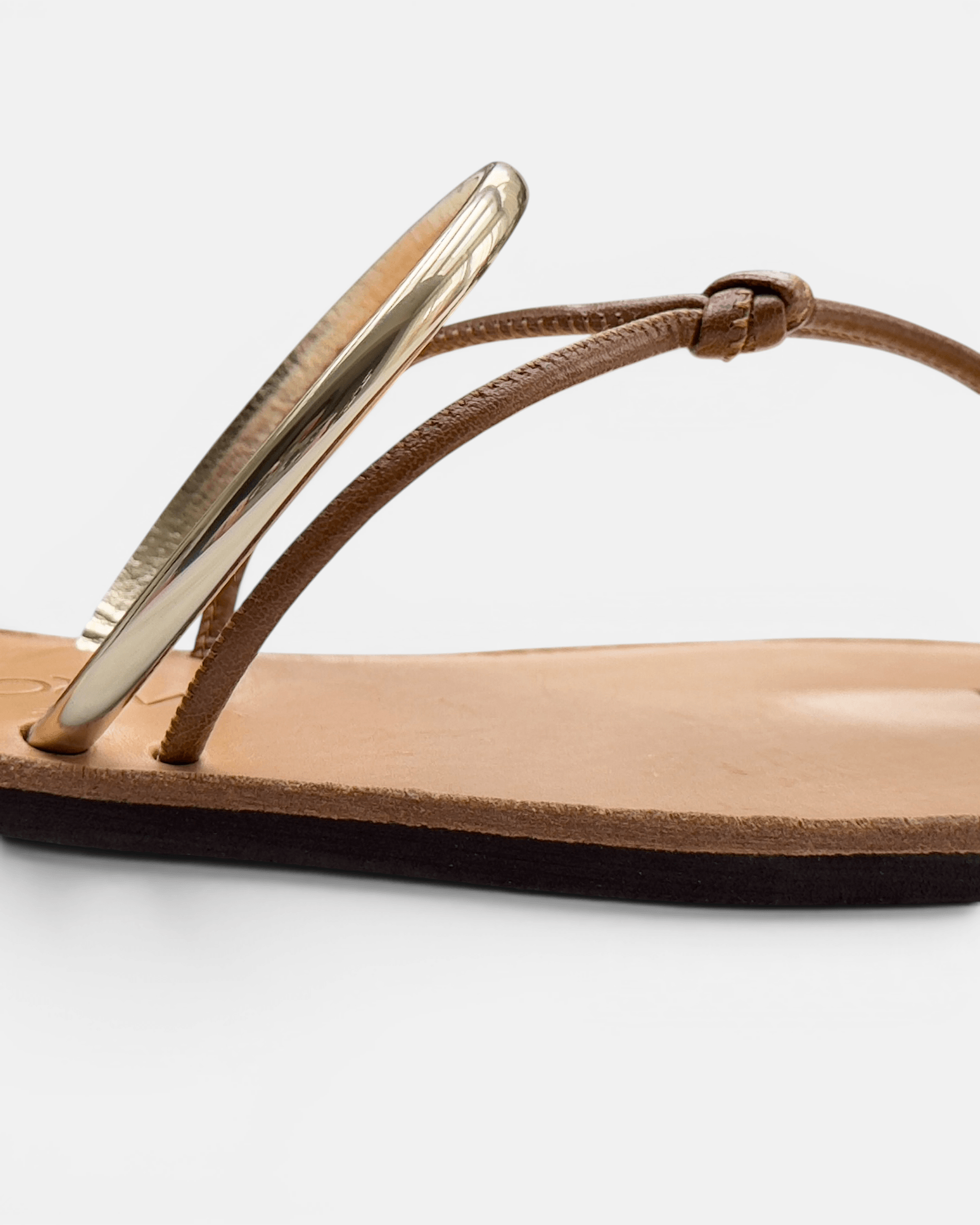 Brown sandal with a gold toe ring on a white background