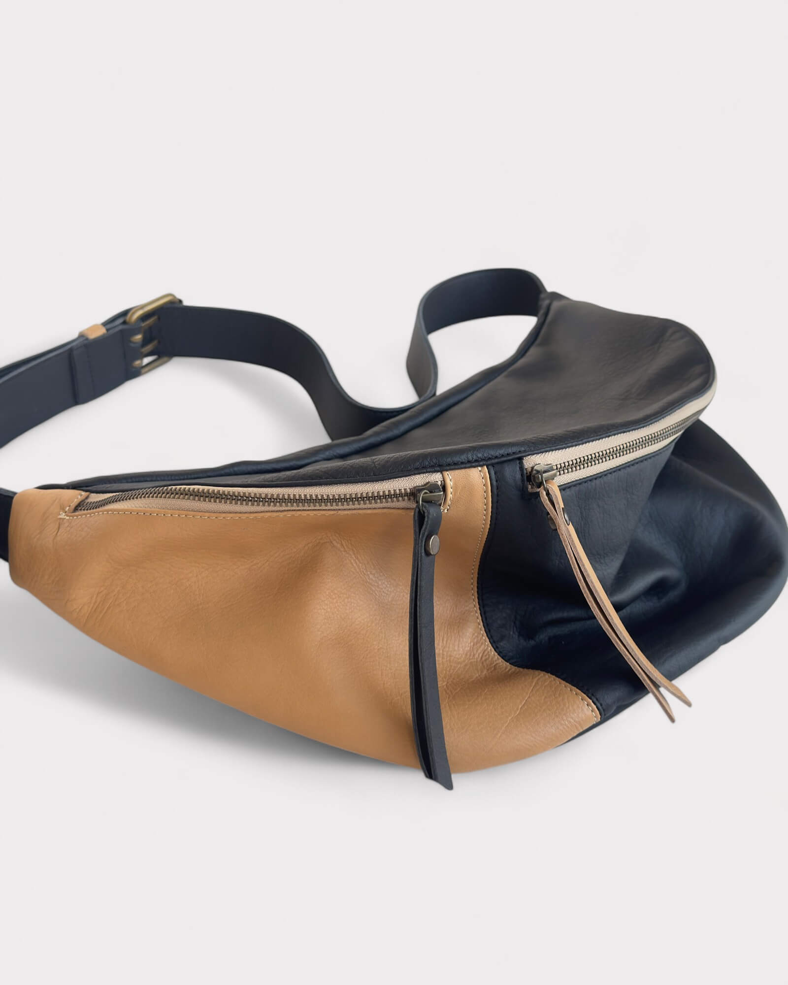 Two-toned black and tan leather waist bag on a light gray background
