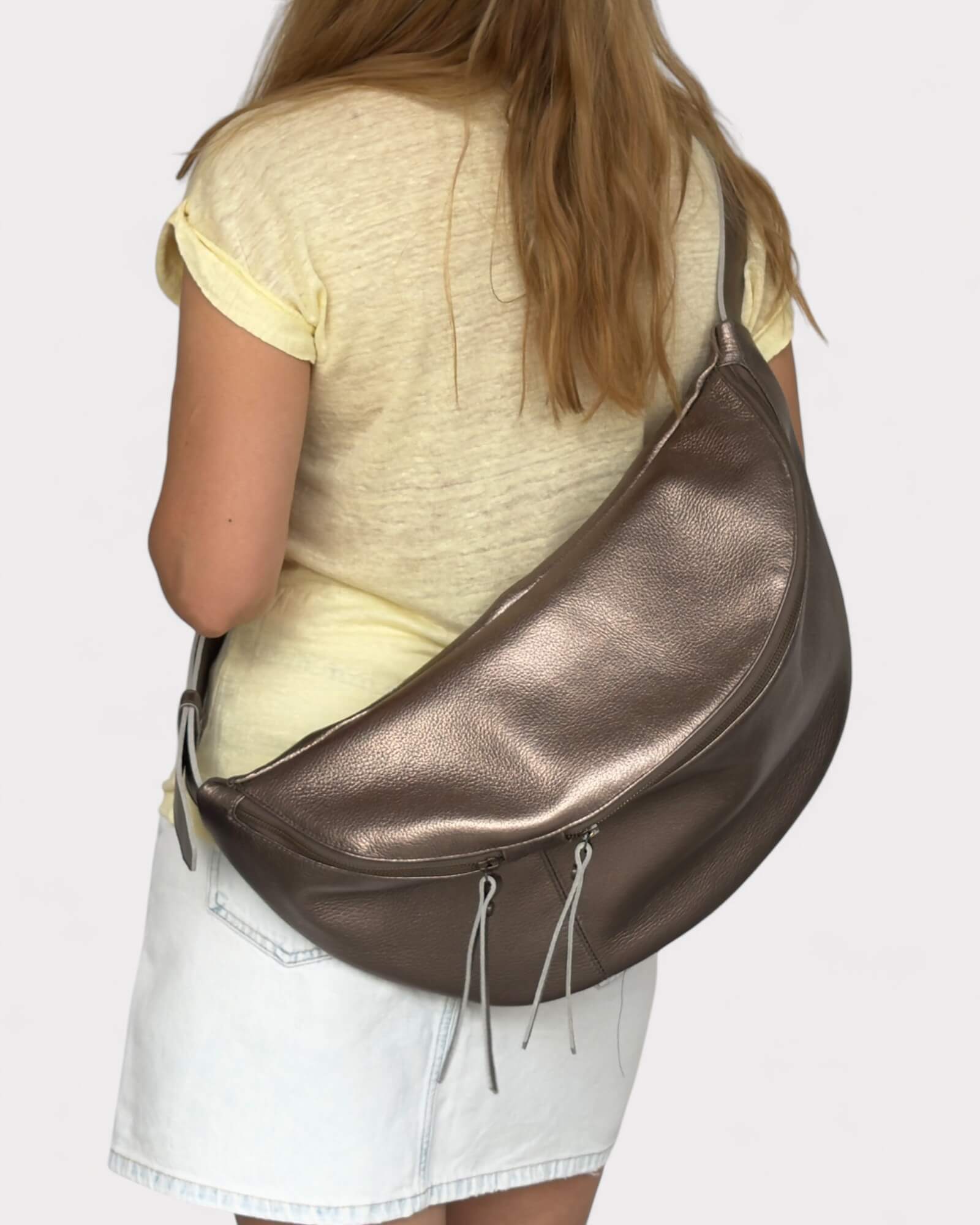 Person wearing a metallic bronze leather sling bag on a plain background