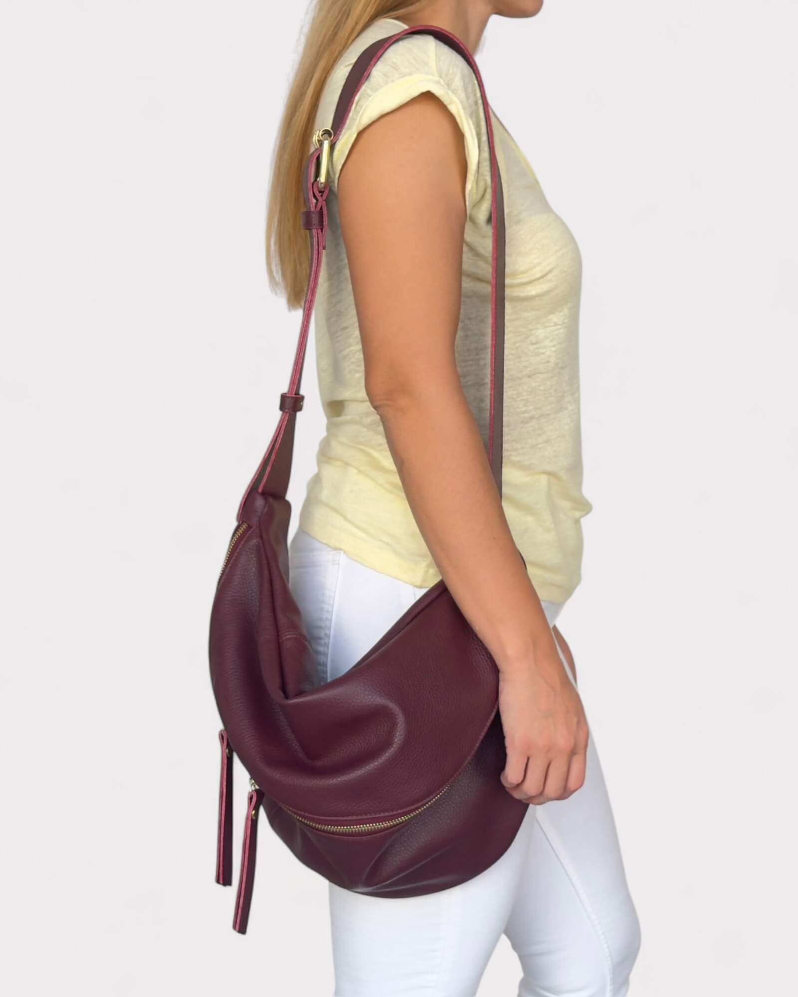 Model wearing a burgundy leather handbag on a plain background