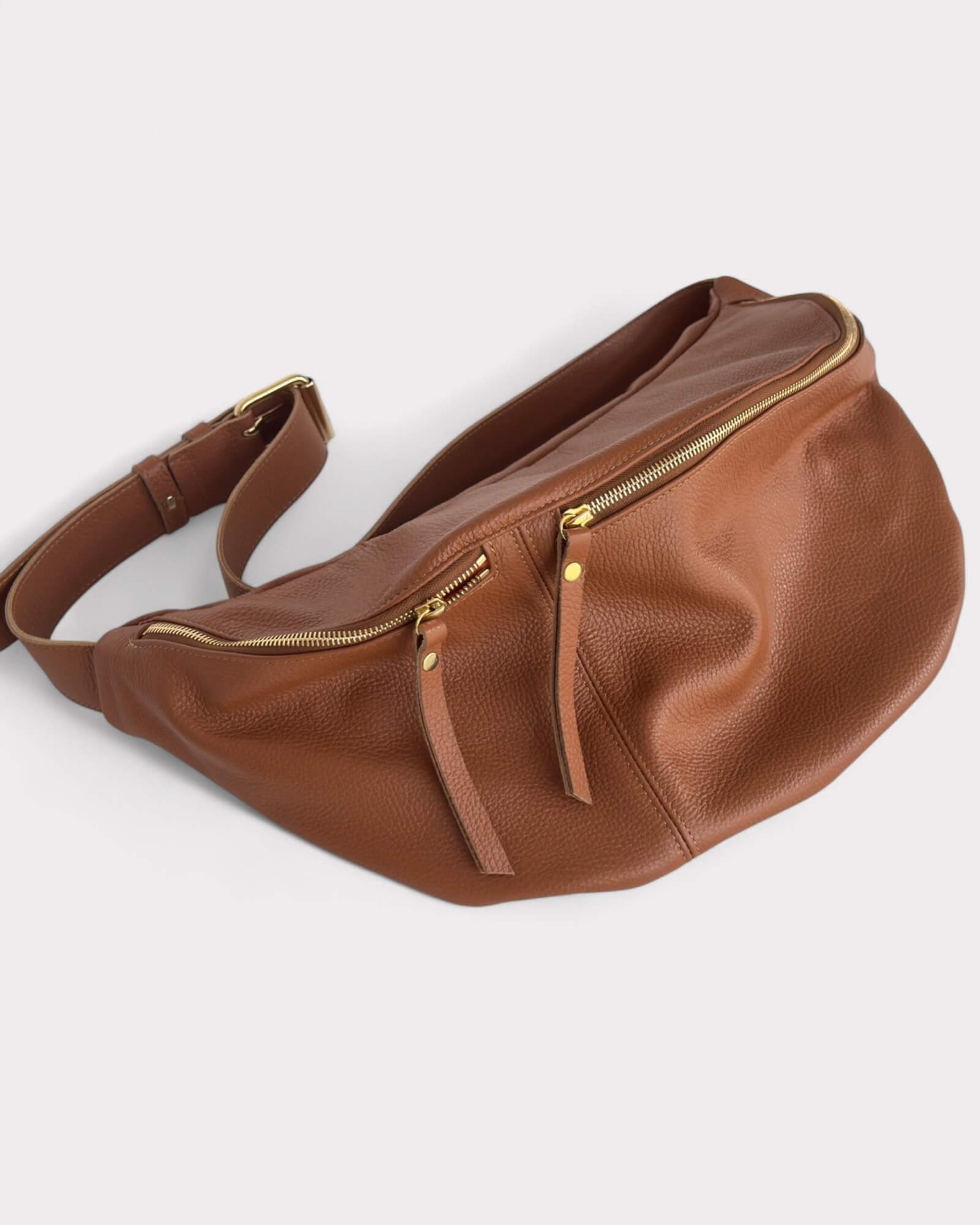 Tan leather waist bag with gold zippers on a white background