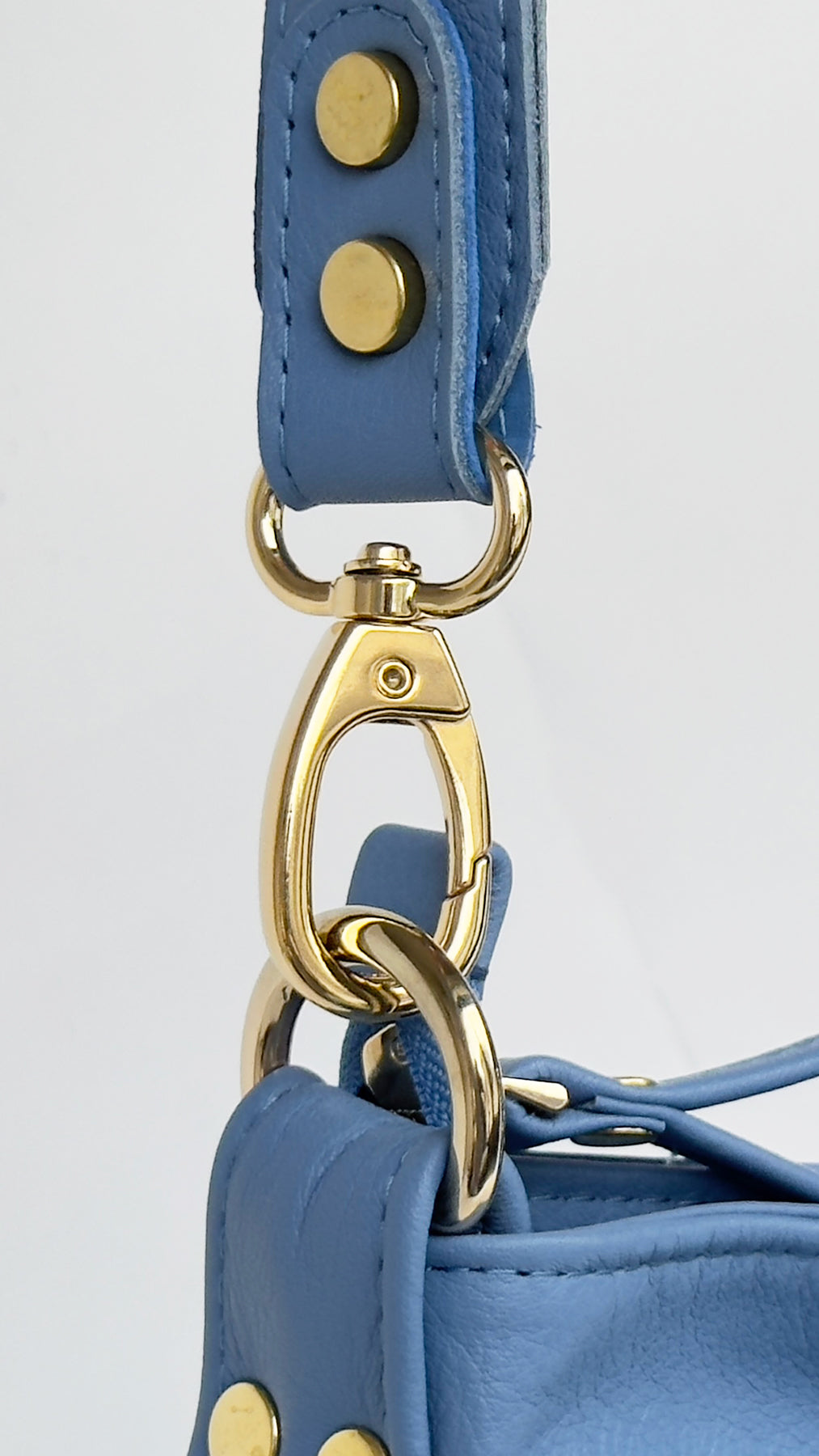 Close-up of a blue handbag with gold hardware on a light gray background