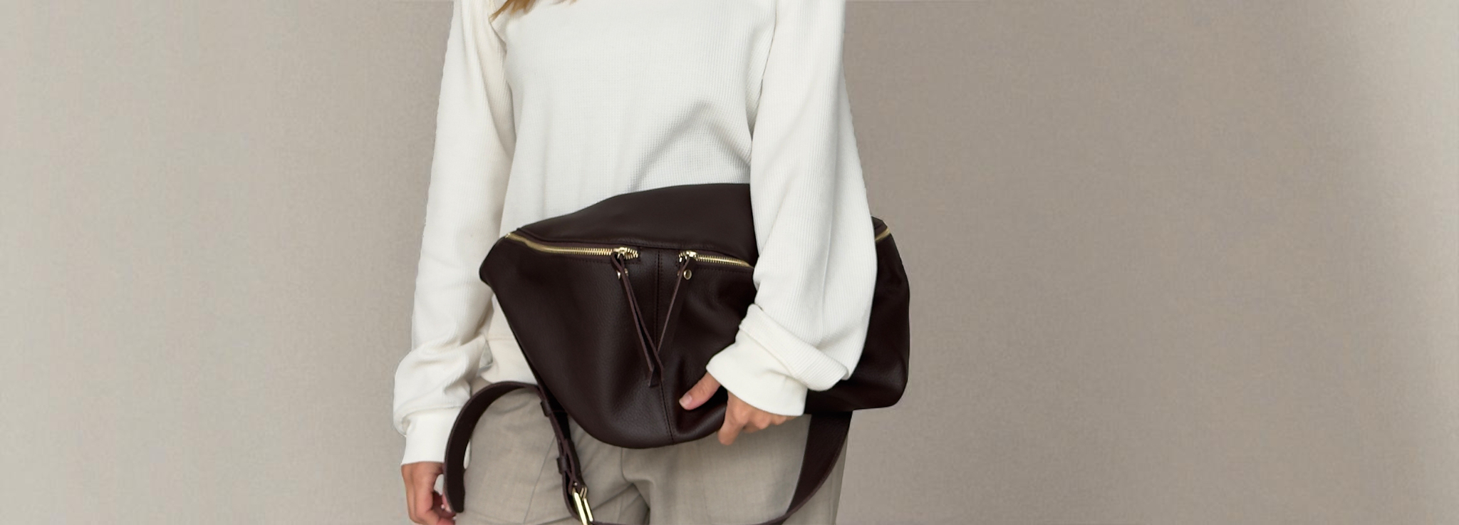 Person wearing a white sweater and carrying a brown leather bag on a plain background