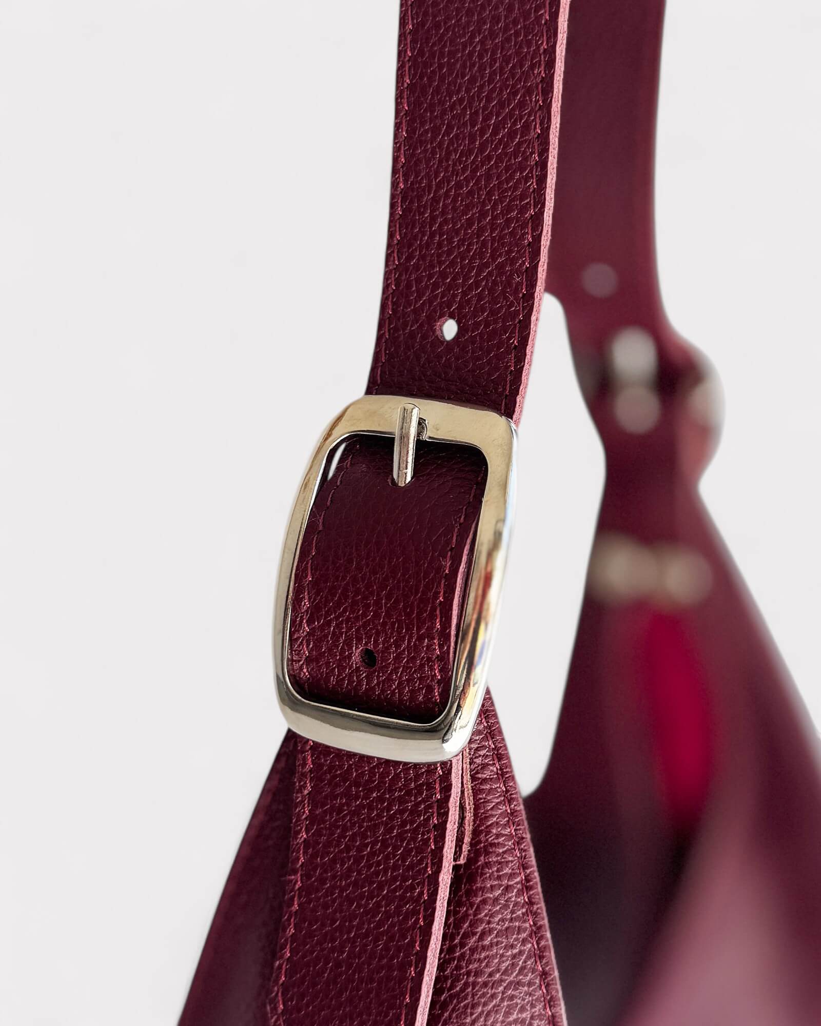 Close-up of a burgundy leather strap with a nickel buckle on a white background
