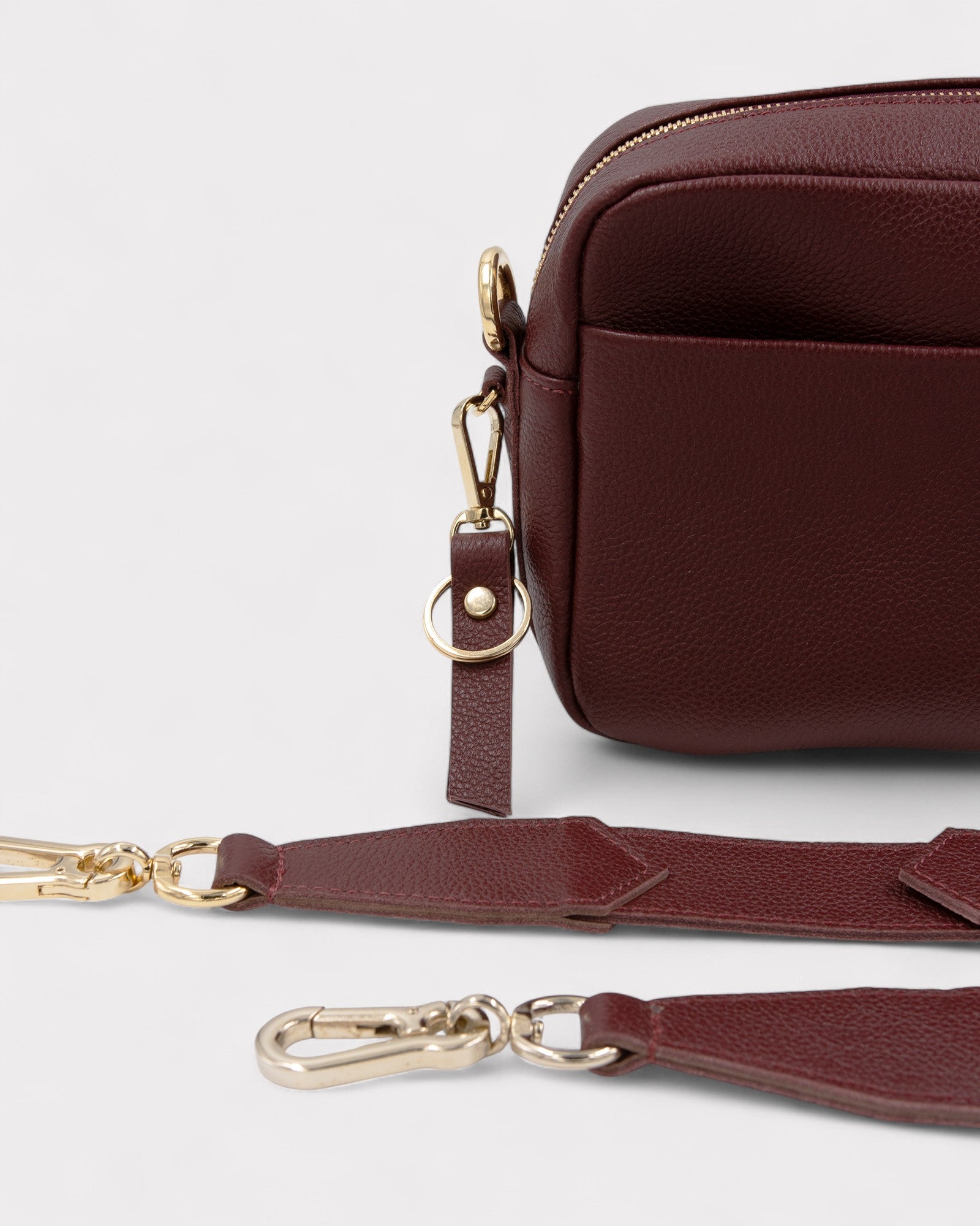 Burgundy leather bag with gold hardware on a light gray background