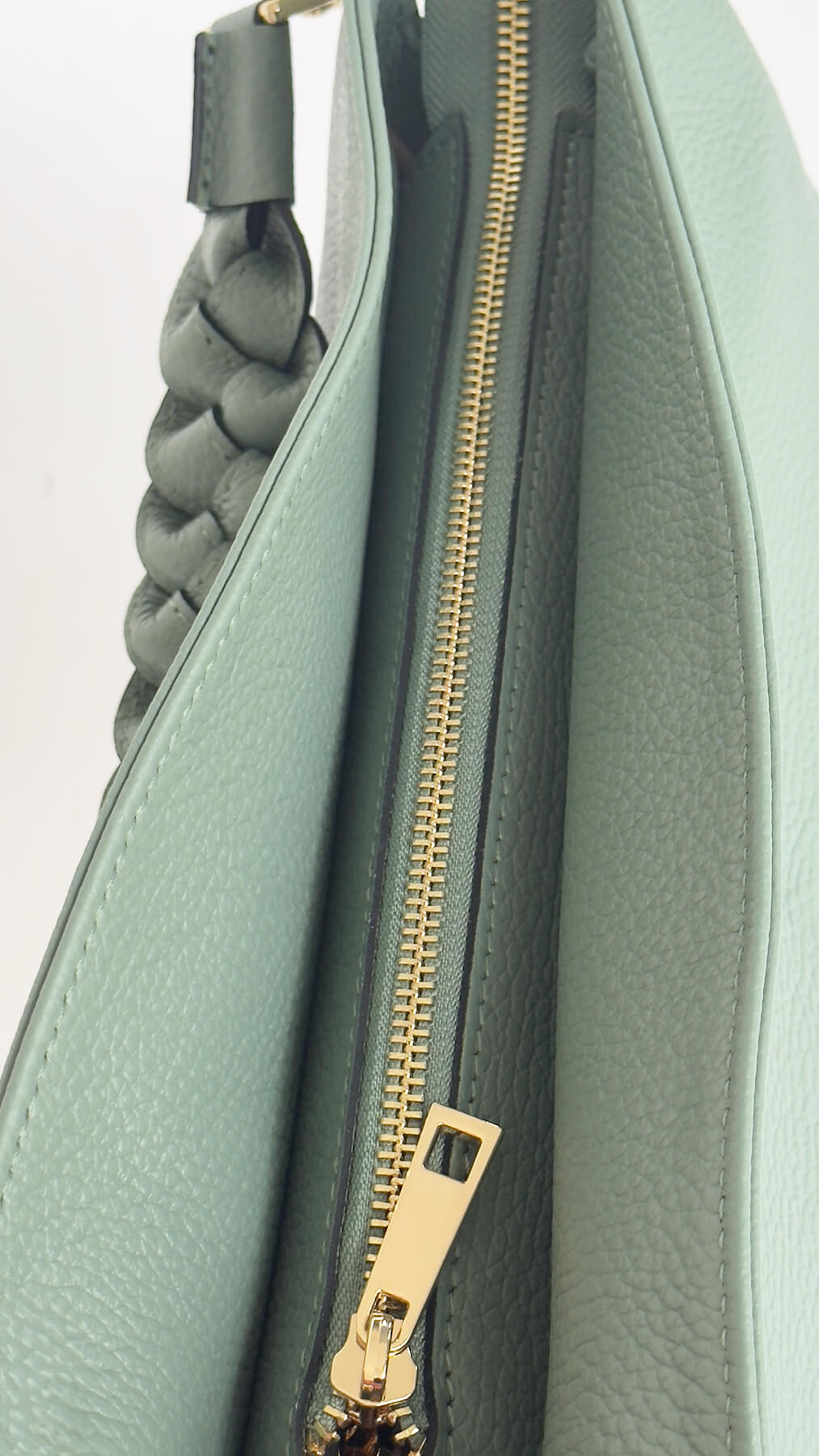 Green handbag with braided handle and gold zipper on a light gray background