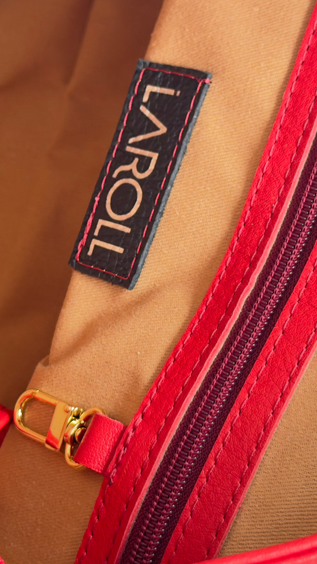 Close-up of a brown leather bag with a red zipper and 'Larroll' brand label.