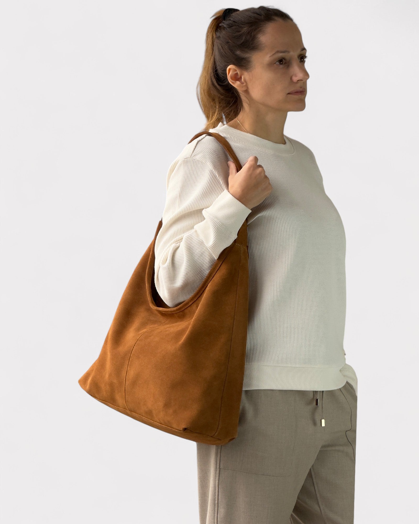 Woman holding a tan leather tote bag against a plain background